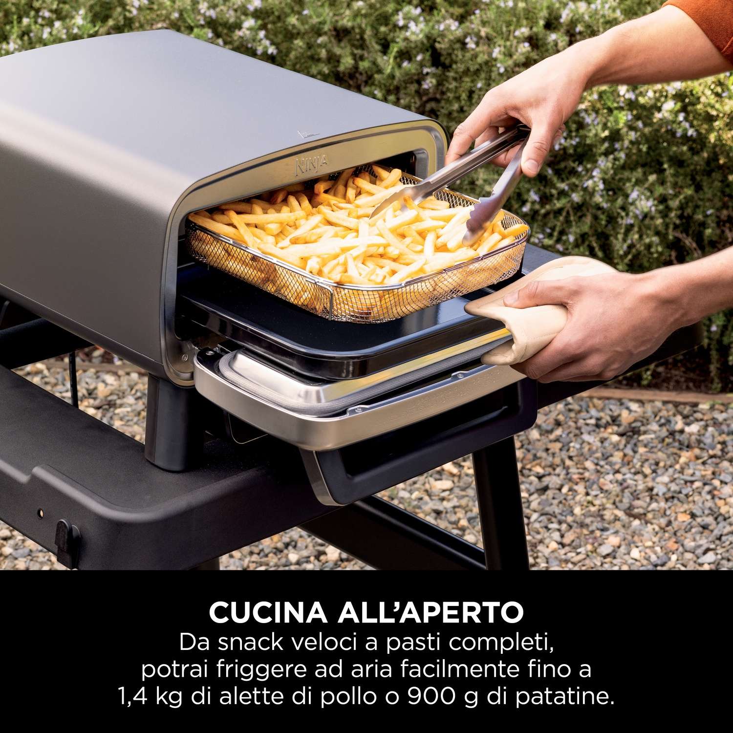 Una persona usa le pinze per rimuovere le patatine fritte da una friggitrice ad aria. La friggitrice è su una superficie nera con testo.