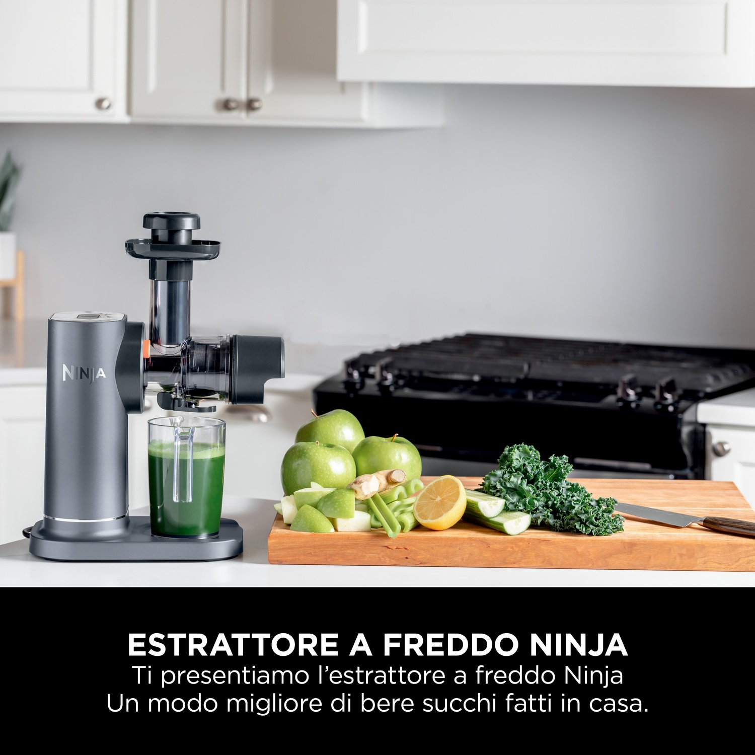 Un estrattore di succo a freddo Ninja con un bicchiere di succo verde. Mele, limone e verdure su un tagliere di legno. Cucina bianca.