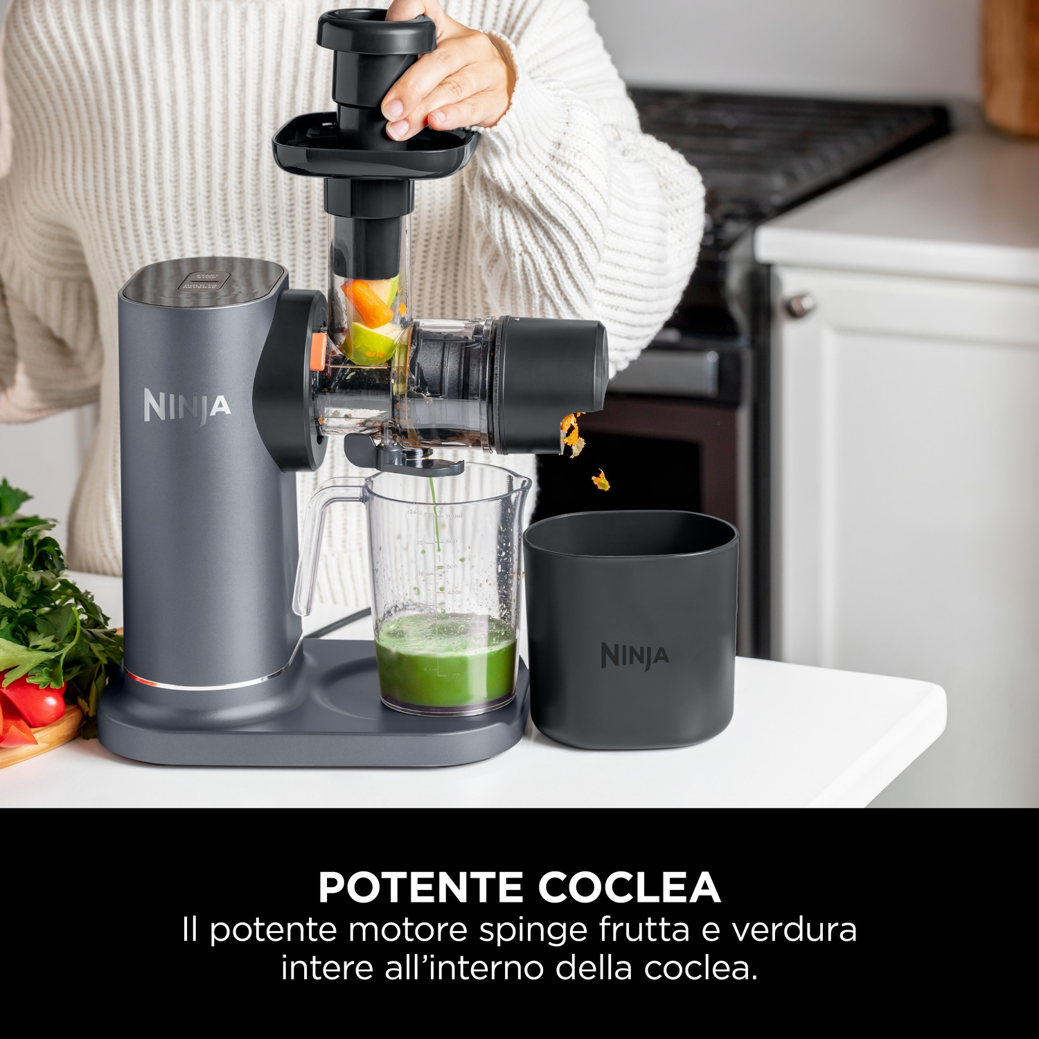 Una persona usa un estrattore di succo Ninja. La frutta viene spremuta. Il succo verde riempie un contenitore. L'estrattore è su una superficie bianca.