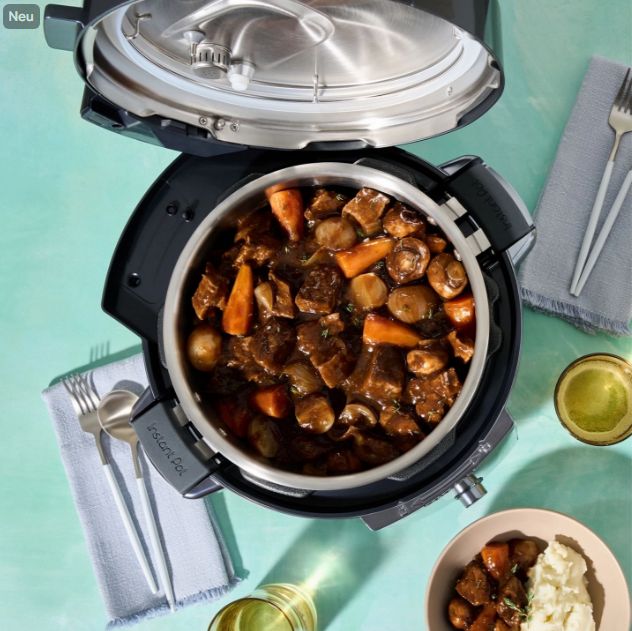 Ein Instant Pot mit Rindfleisch-Eintopf, Karotten und Pilzen. Serviert mit Kartoffelpüree und Besteck auf einer türkisfarbenen Oberfläche.