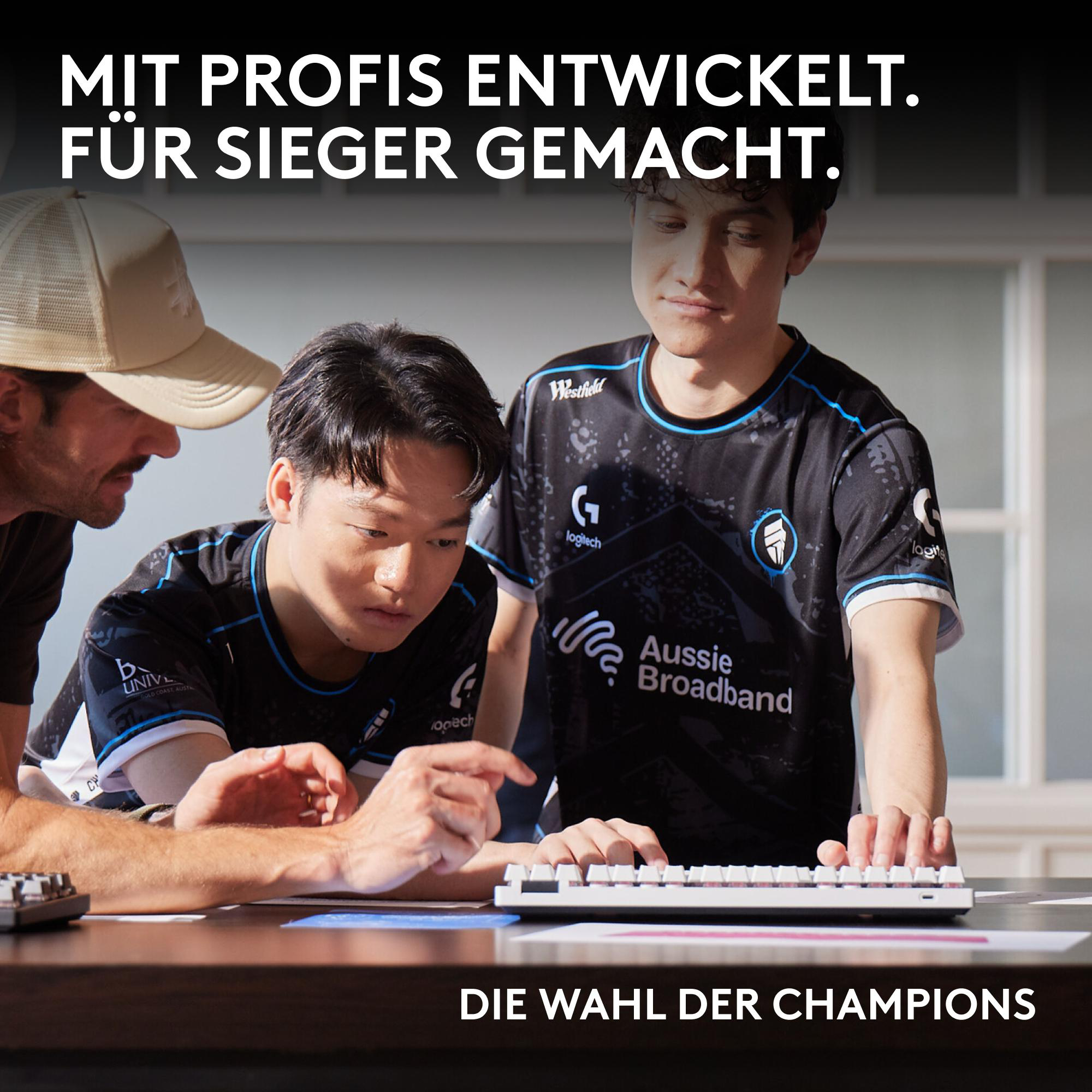Drei E-Sportler betrachten eine Tastatur. Der Text lautet: 'Von Profis entwickelt. Für Sieger gemacht. Die Wahl der Champions.'