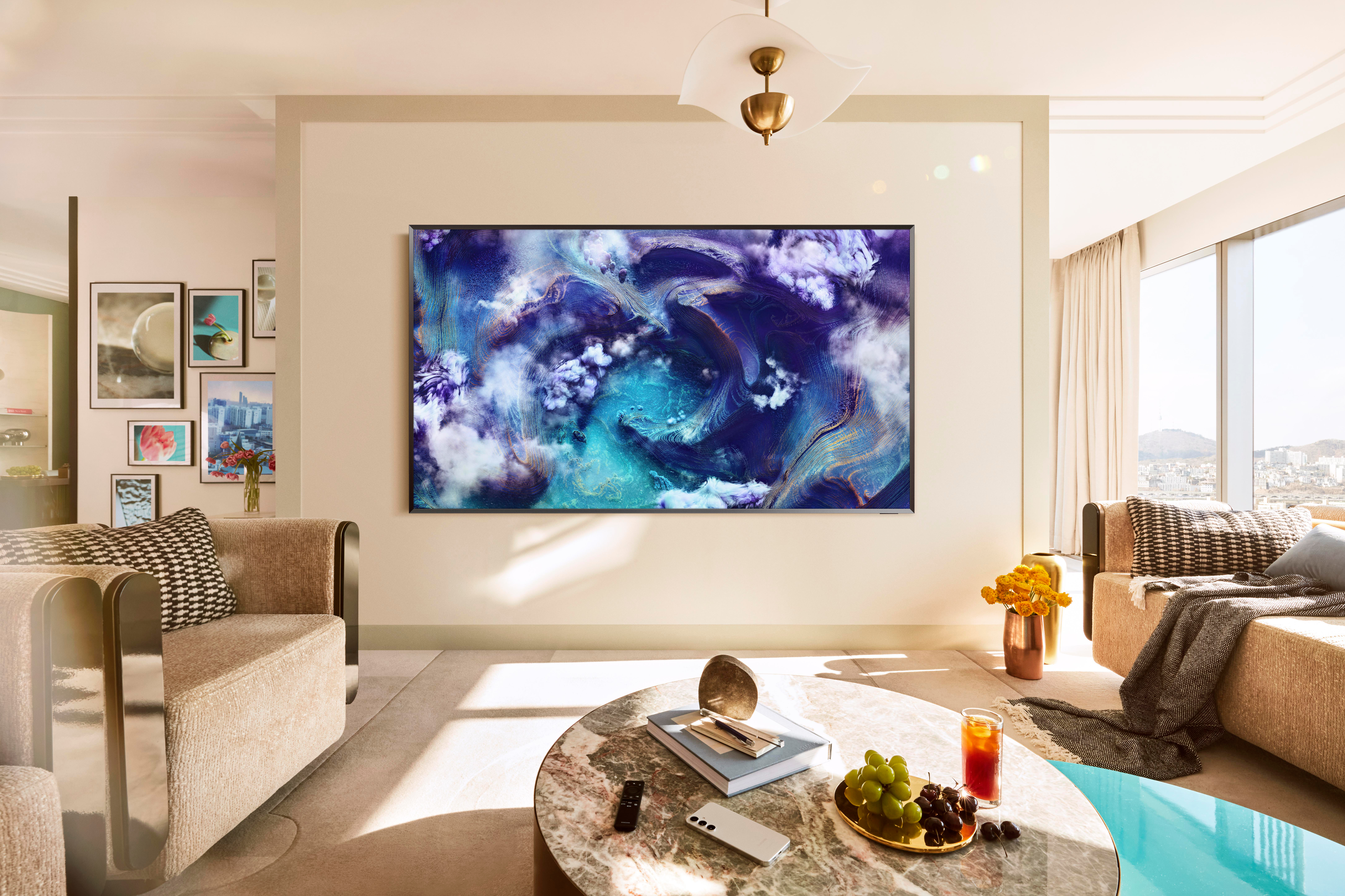 Wohnzimmer mit großem Fernseher mit abstraktem Kunstwerk. Sofas, Couchtisch mit Obst und Getränken und Stadtblick durch das Fenster.