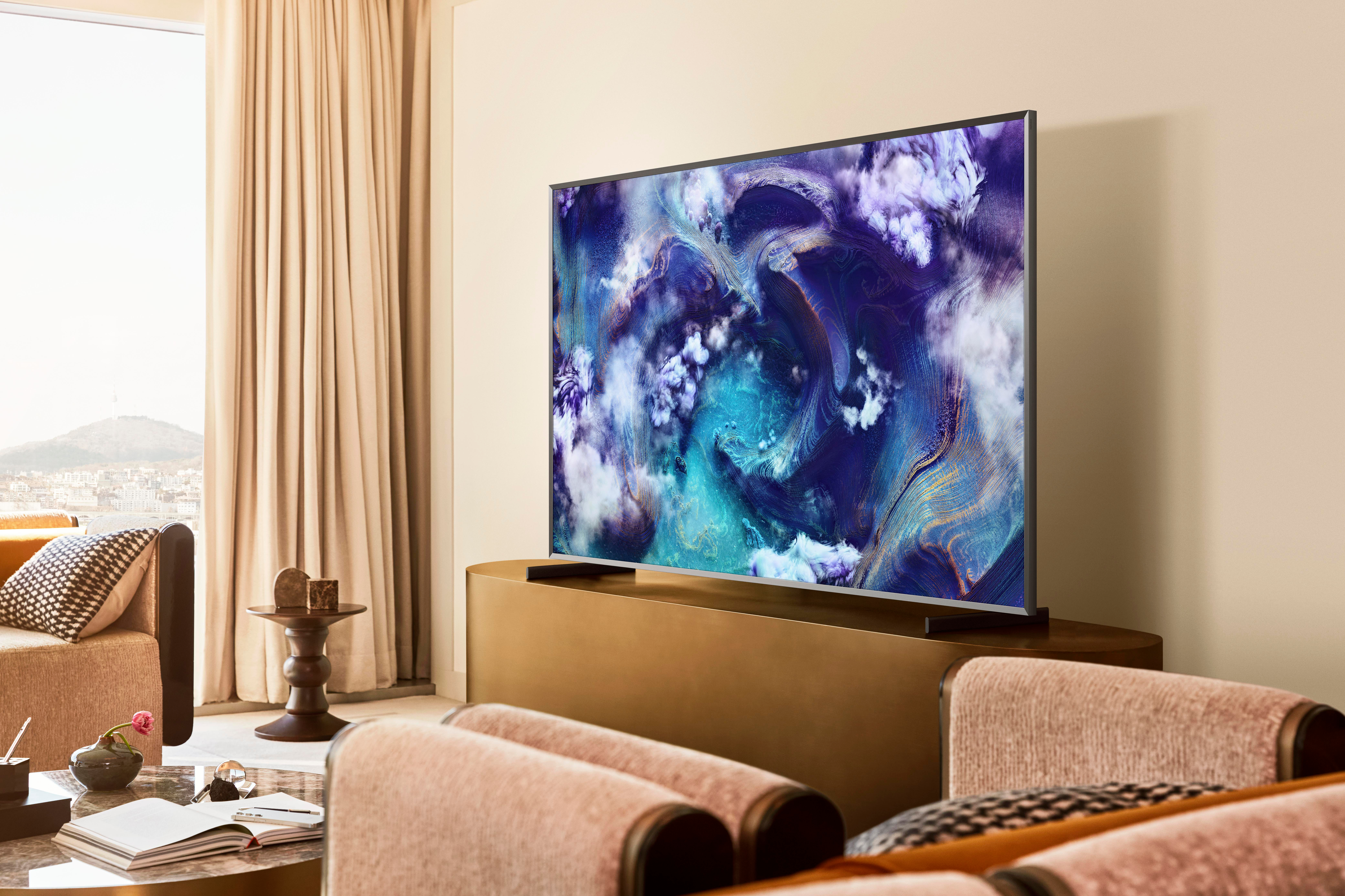 Wohnzimmer mit großem Fernseher mit blauem abstraktem Kunstwerk. Beige Möbel und Vorhänge. Blick auf die Stadt durch das Fenster.