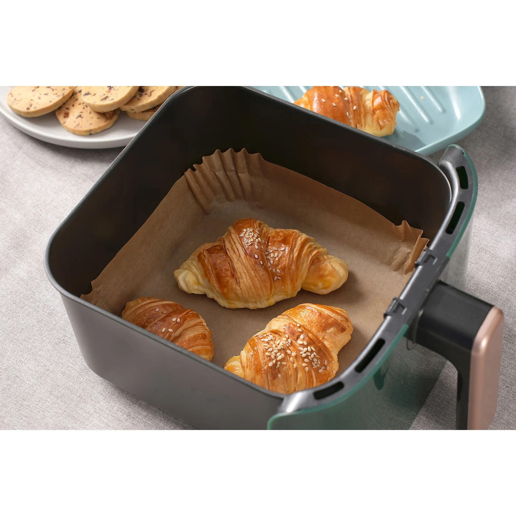 Frytkownica powietrzna z rogalikami w środku. Ciasteczka na talerzu i rogalik na niebieskim talerzu są również widoczne.