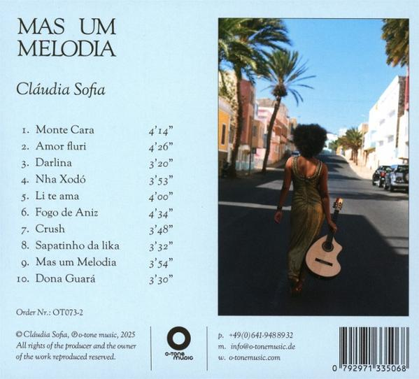 Eine Frau mit Afro geht eine Straße entlang und hält eine Gitarre. Gebäude und Palmen säumen die Straße unter blauem Himmel.