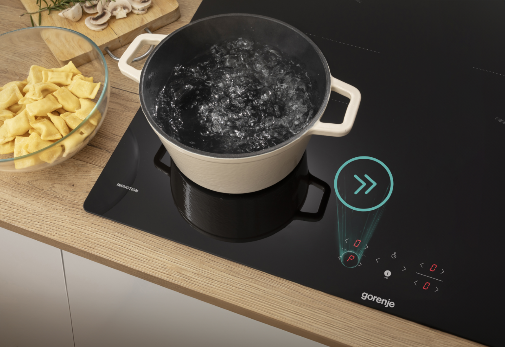 Garnek wrzącej wody na czarnej płycie indukcyjnej, z miską makaronu i składnikami w tle.
