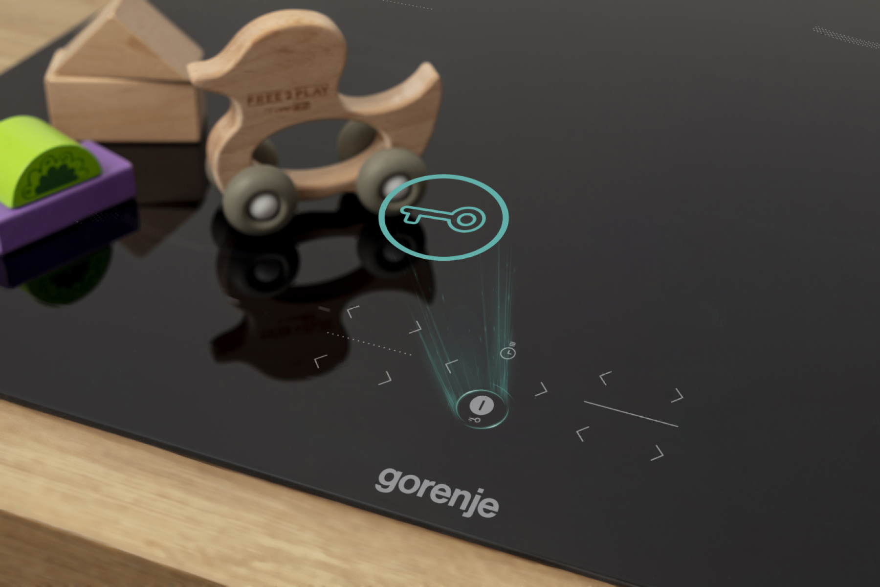 Czarna płyta kuchenna z klockami i drewnianym samochodem. Ikona klucza się podświetla. Widoczna jest marka 'gorenje'.