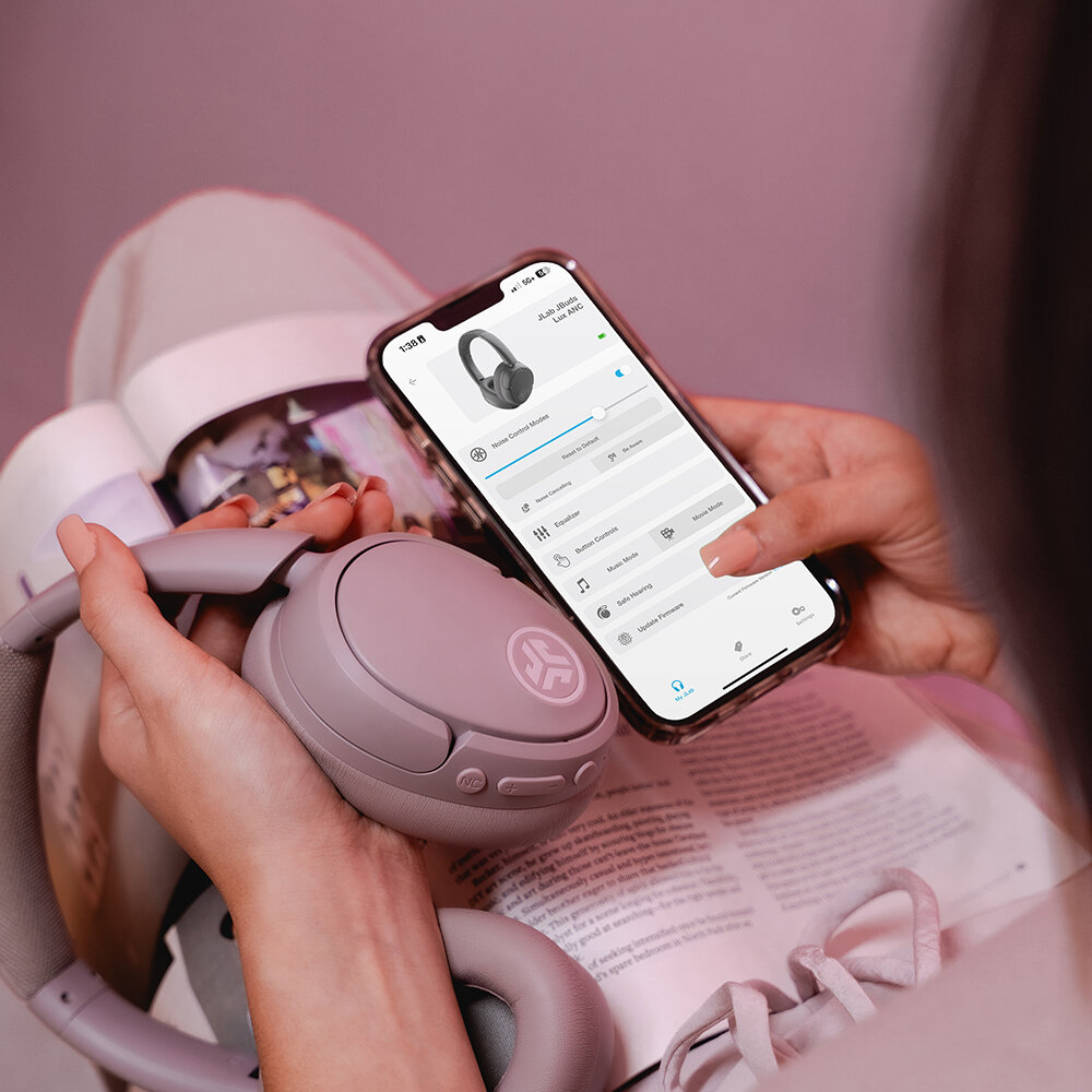 Osoba trzyma bezprzewodowe słuchawki i smartfon. Telefon wyświetla ustawienia słuchawek. W tle znajduje się magazyn.