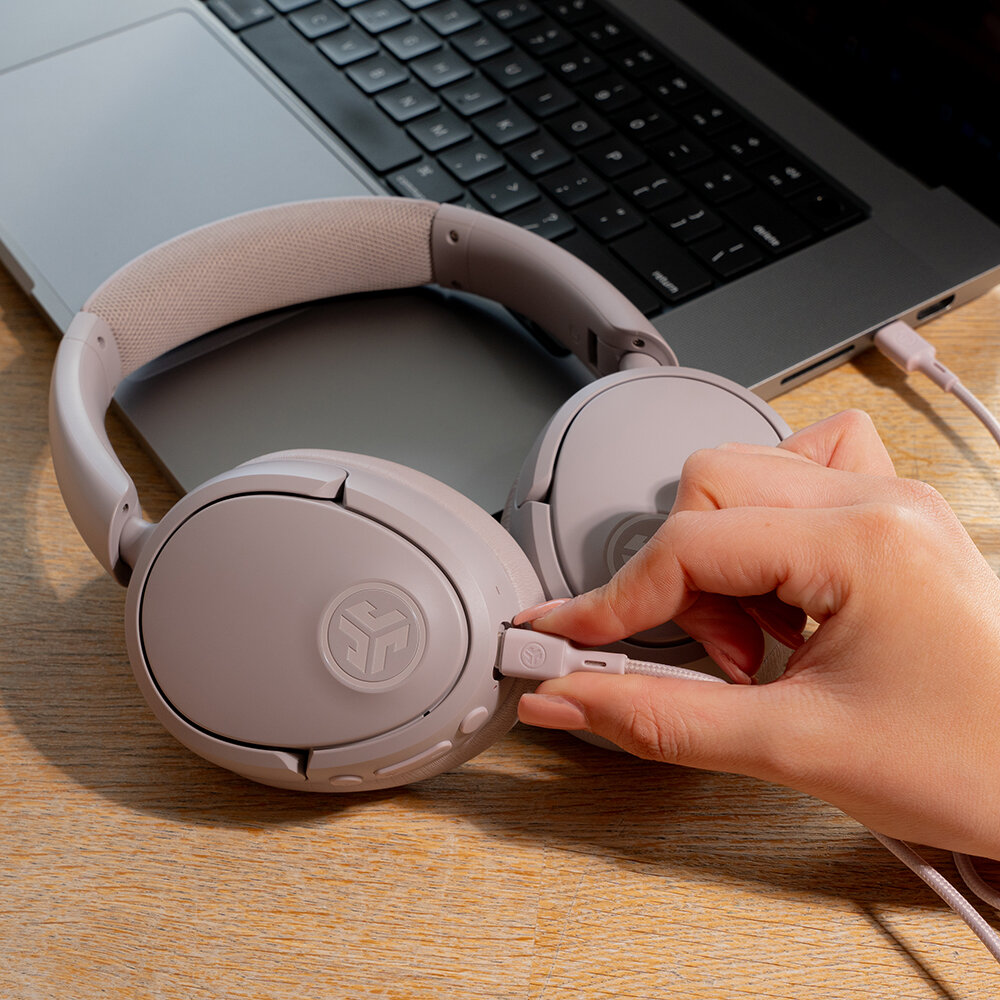 Osoba podłącza fioletowe słuchawki do laptopa. Słuchawki leżą na drewnianej powierzchni.