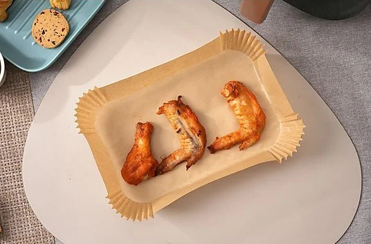 Trzy smażone skrzydełka z kurczaka na papierowej tacy, plus taca ciasteczek. Umieszczone na białej powierzchni z szarym tłem tekstylnym.