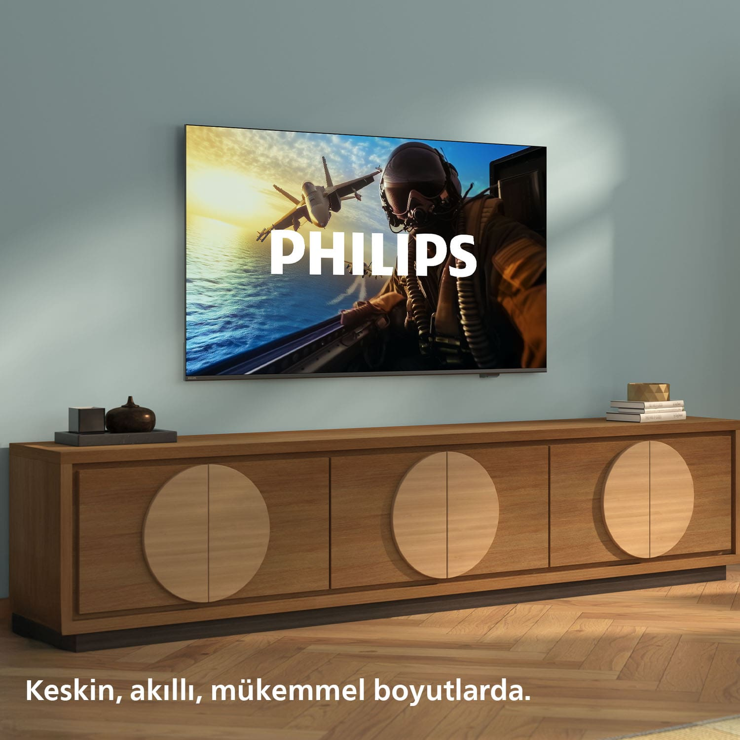 Bir TV, su üzerinde bir jet uçağı gösteriyor. Dairesel detaylara sahip ahşap bir dolabın üzerinde. Ekranda PHILIPS yazısı var.