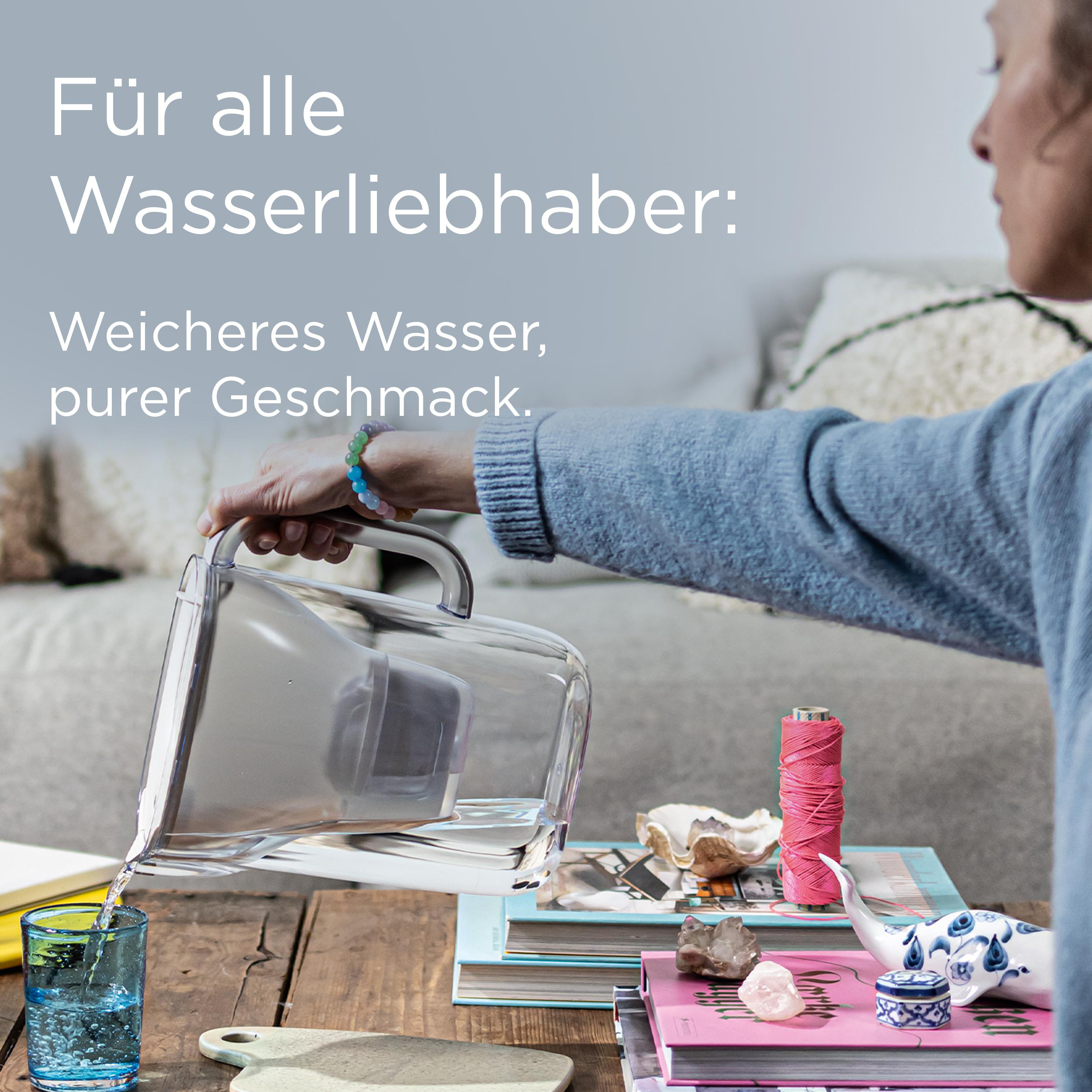 Eine Frau gießt Wasser aus einem Krug in ein Glas. Bücher, eine Garnrolle und Dekor stehen auf einem Holztisch.