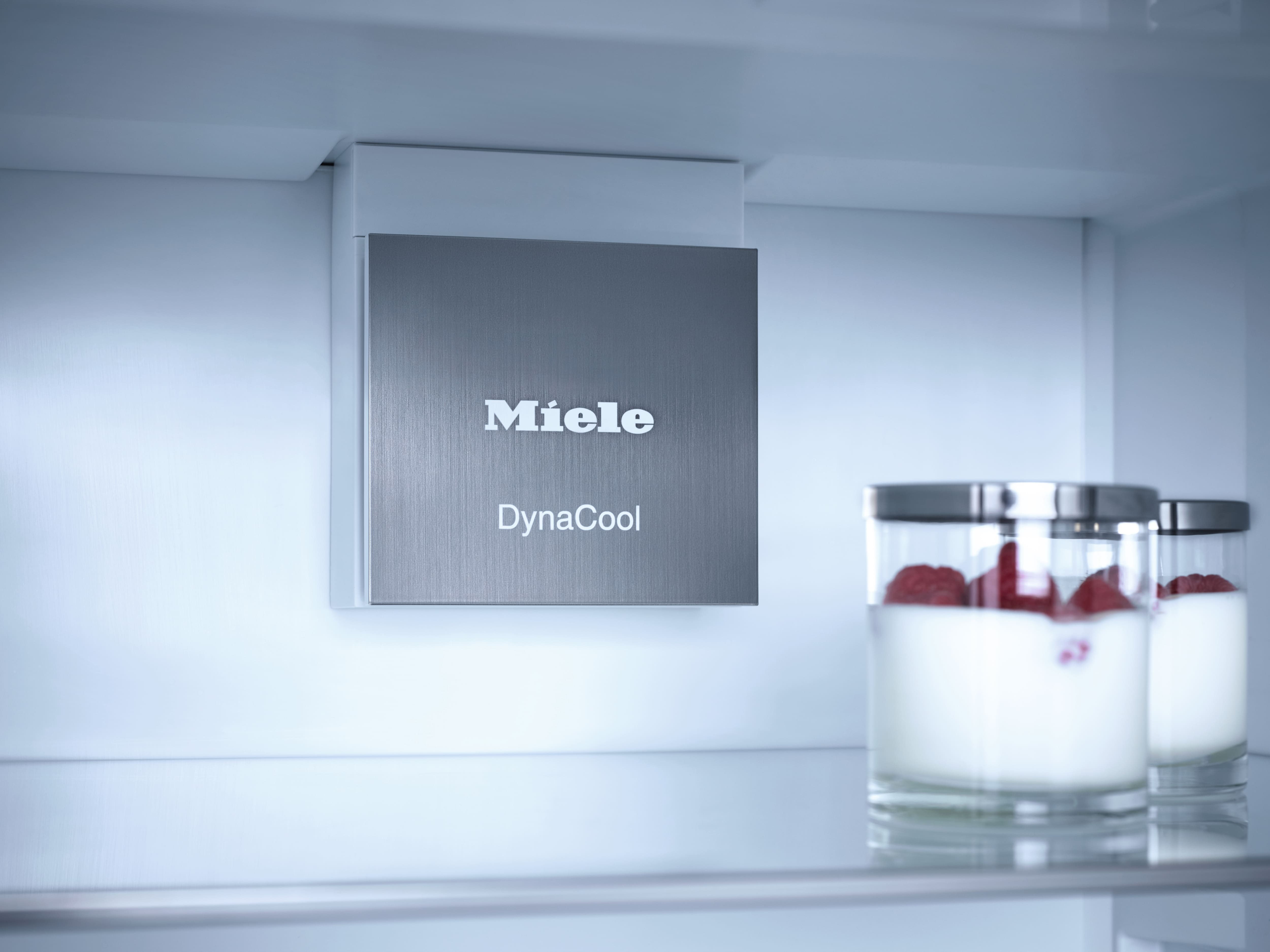 Kühlschrankinnenraum mit Miele-Logo, DynaCool-Etikett und zwei Gläsern mit weißer Flüssigkeit und roten Beeren.