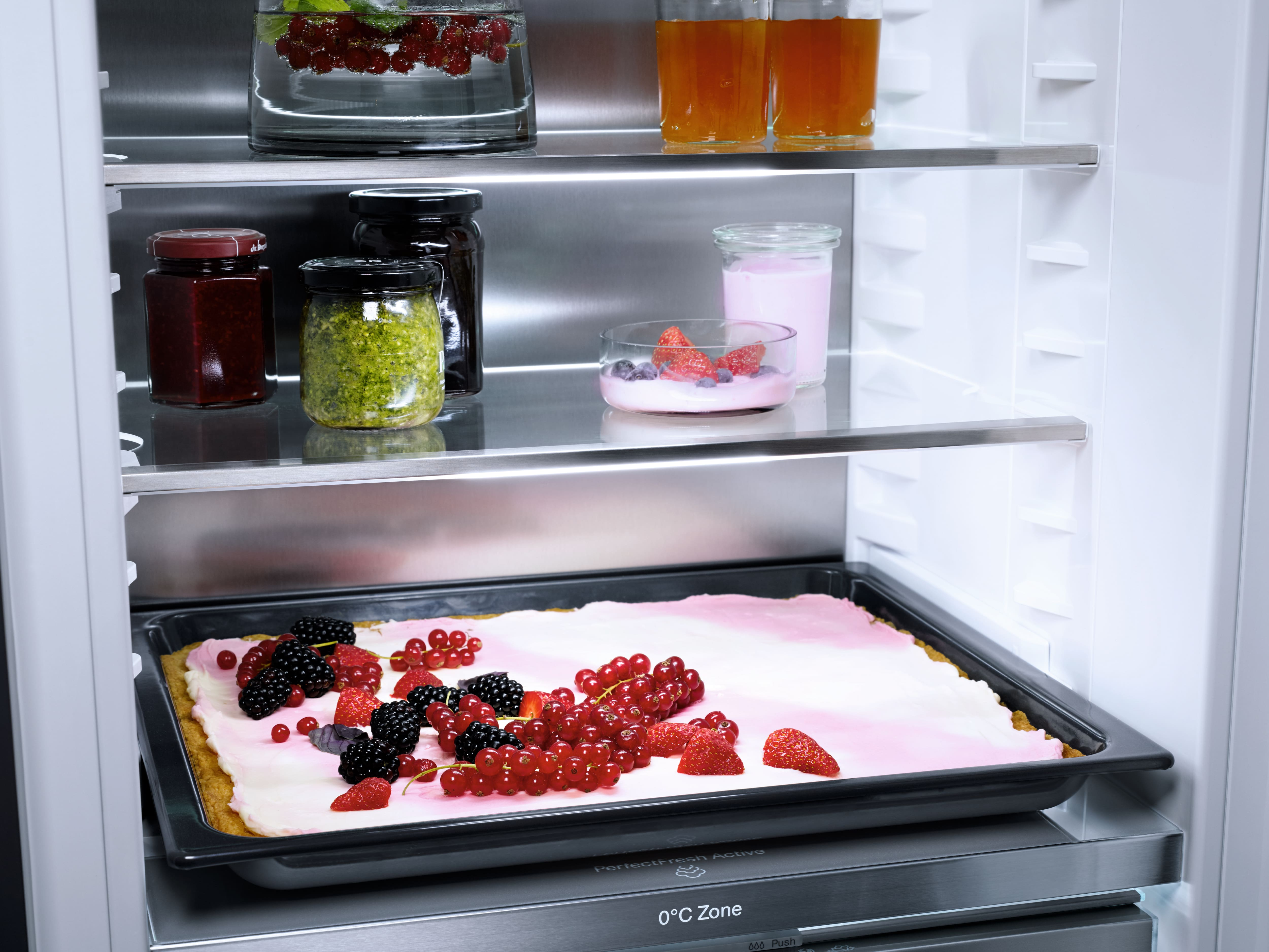 Offener Kühlschrank mit Gläsern, Früchten, Kuchen mit Beeren und Getränken.