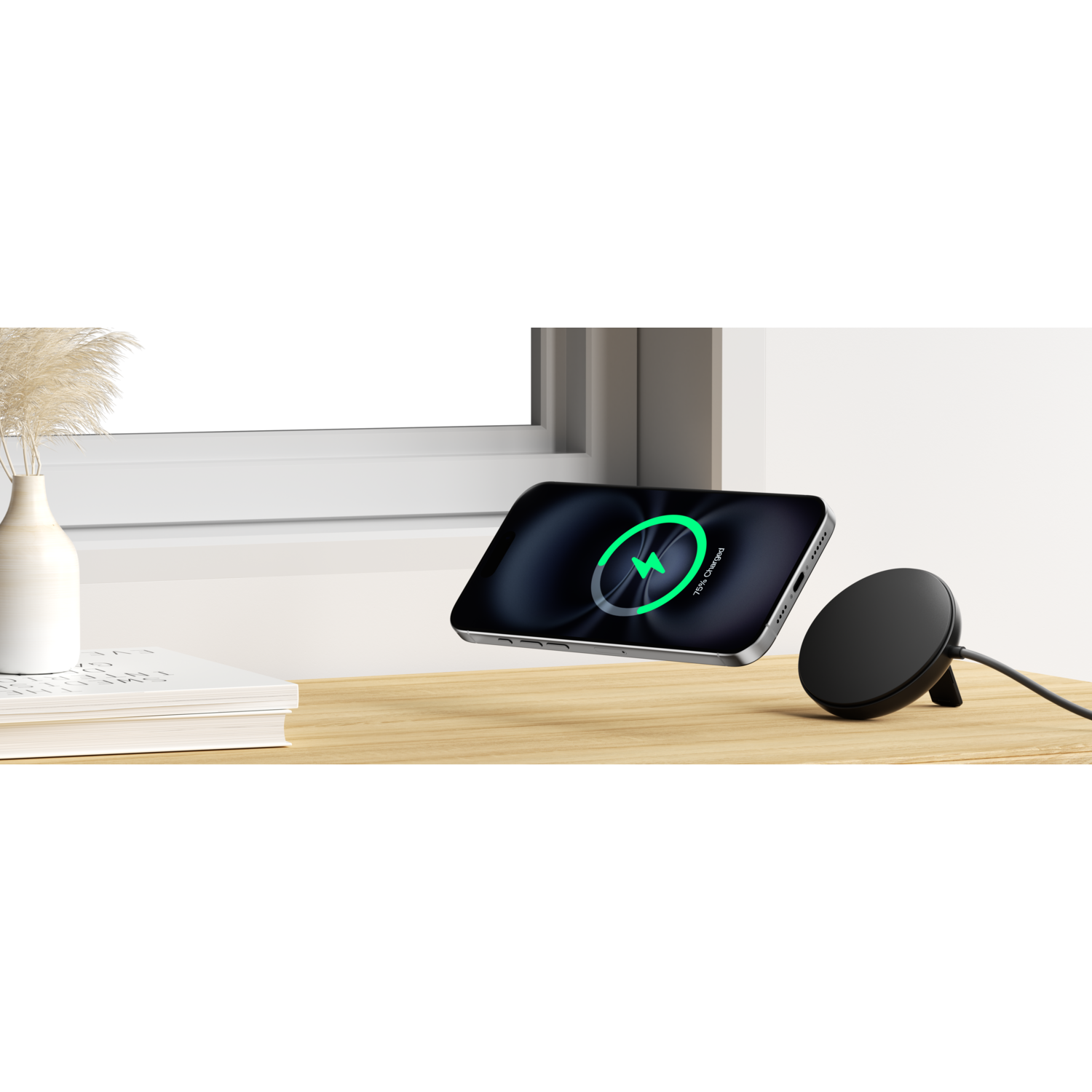 Un téléphone lévite au-dessus d'un bureau en bois, se chargeant sans fil. Un socle de chargement noir est à droite. Un vase et des livres à gauche.