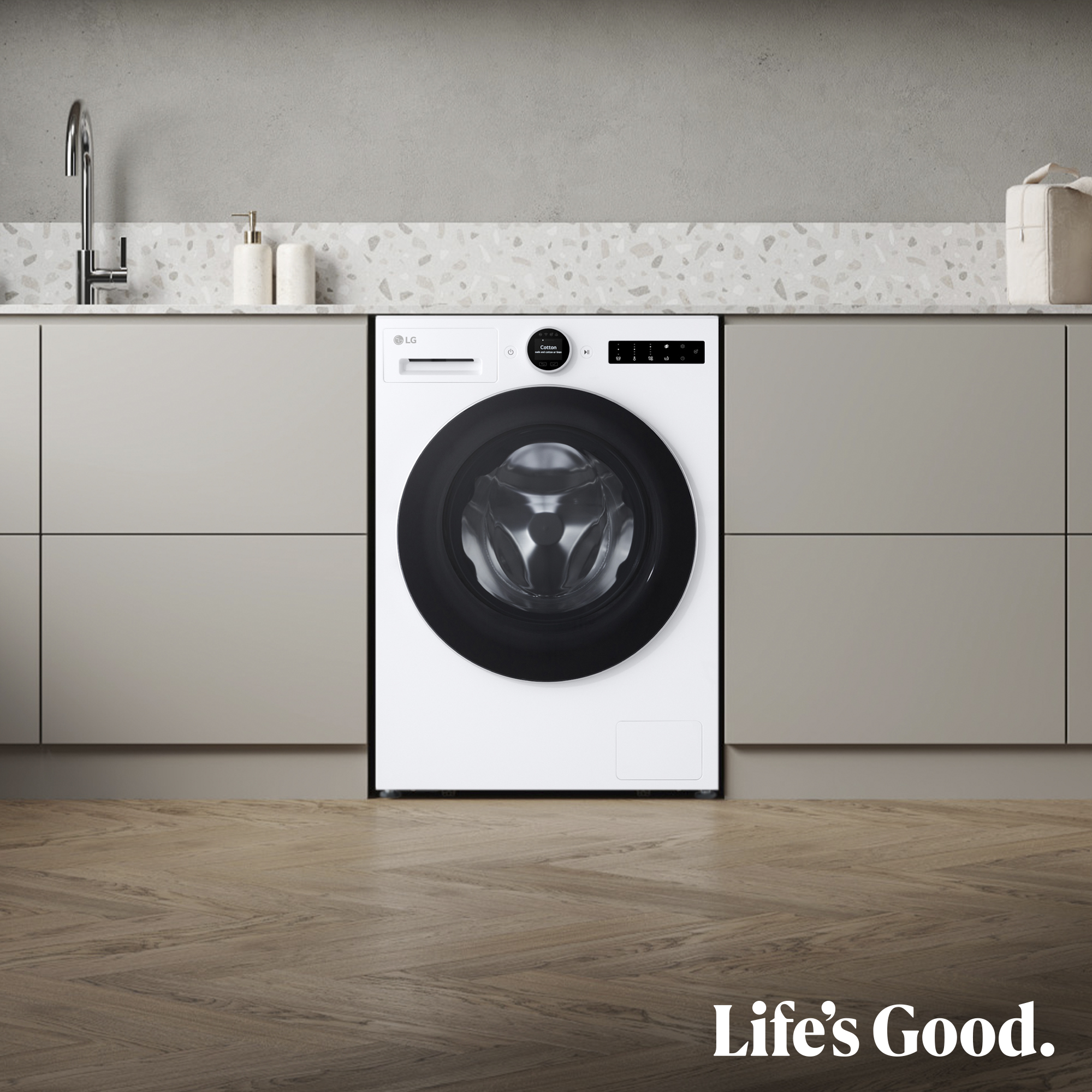 Una lavadora LG blanca centrada en un entorno de cocina. Se ven gabinetes y encimera. "Life's Good" está en la parte inferior.