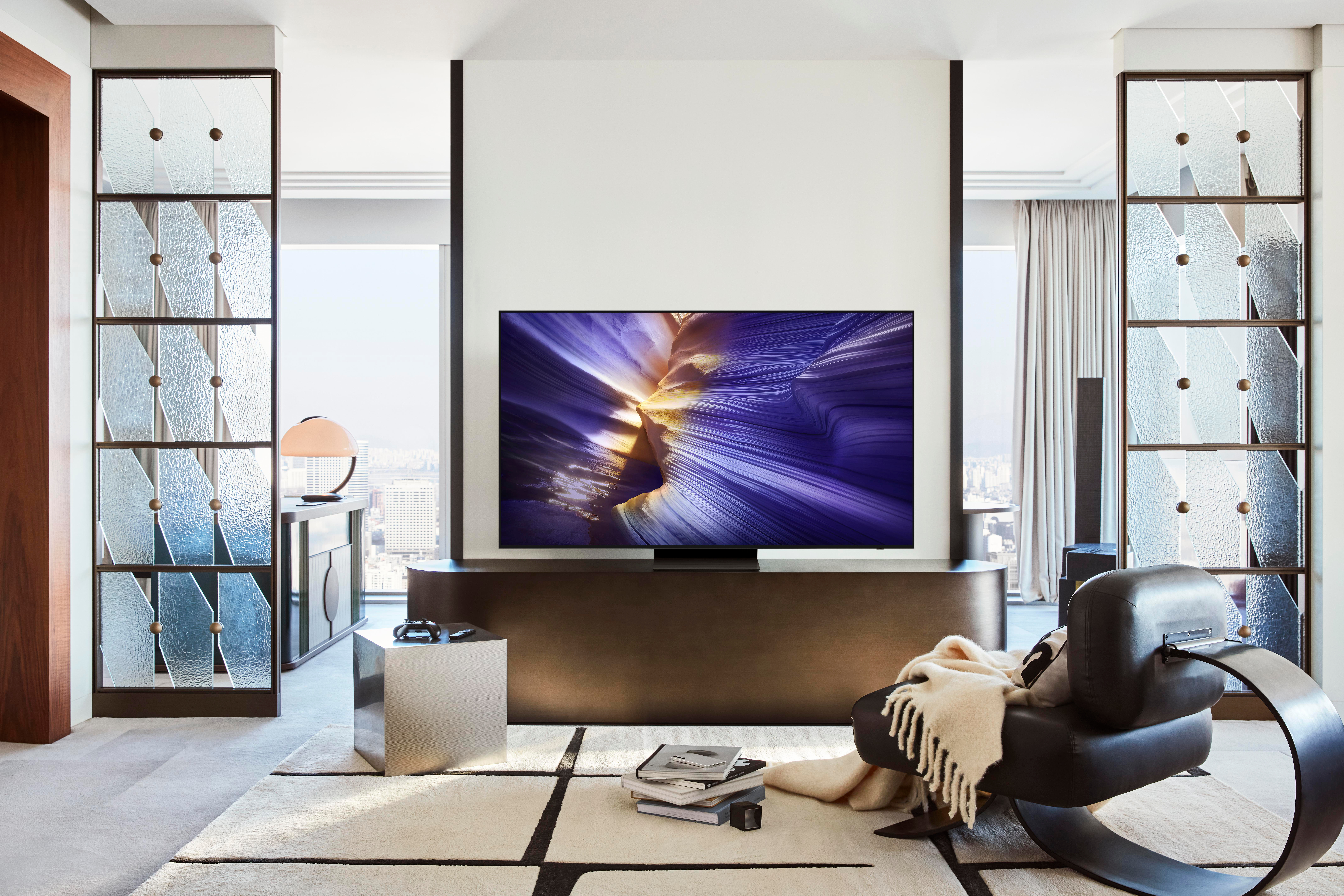 Wohnzimmer mit großem Fernseher, schwarzem Stuhl, Teppich und dekorativen Glaspaneelen. Blick auf die Stadt durch das Fenster.