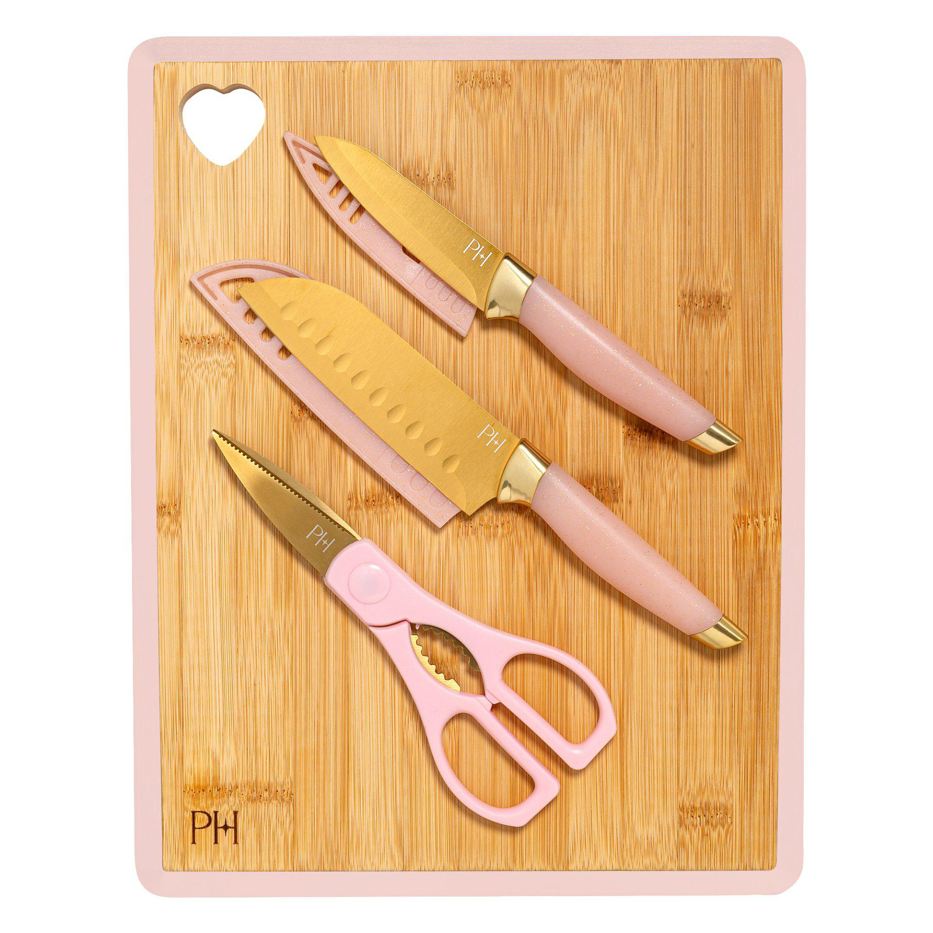 Ein rosa Schneidebrett mit herzförmigem Loch. Drei Küchenwerkzeuge: zwei Messer und eine Schere, alle rosa und goldfarben.