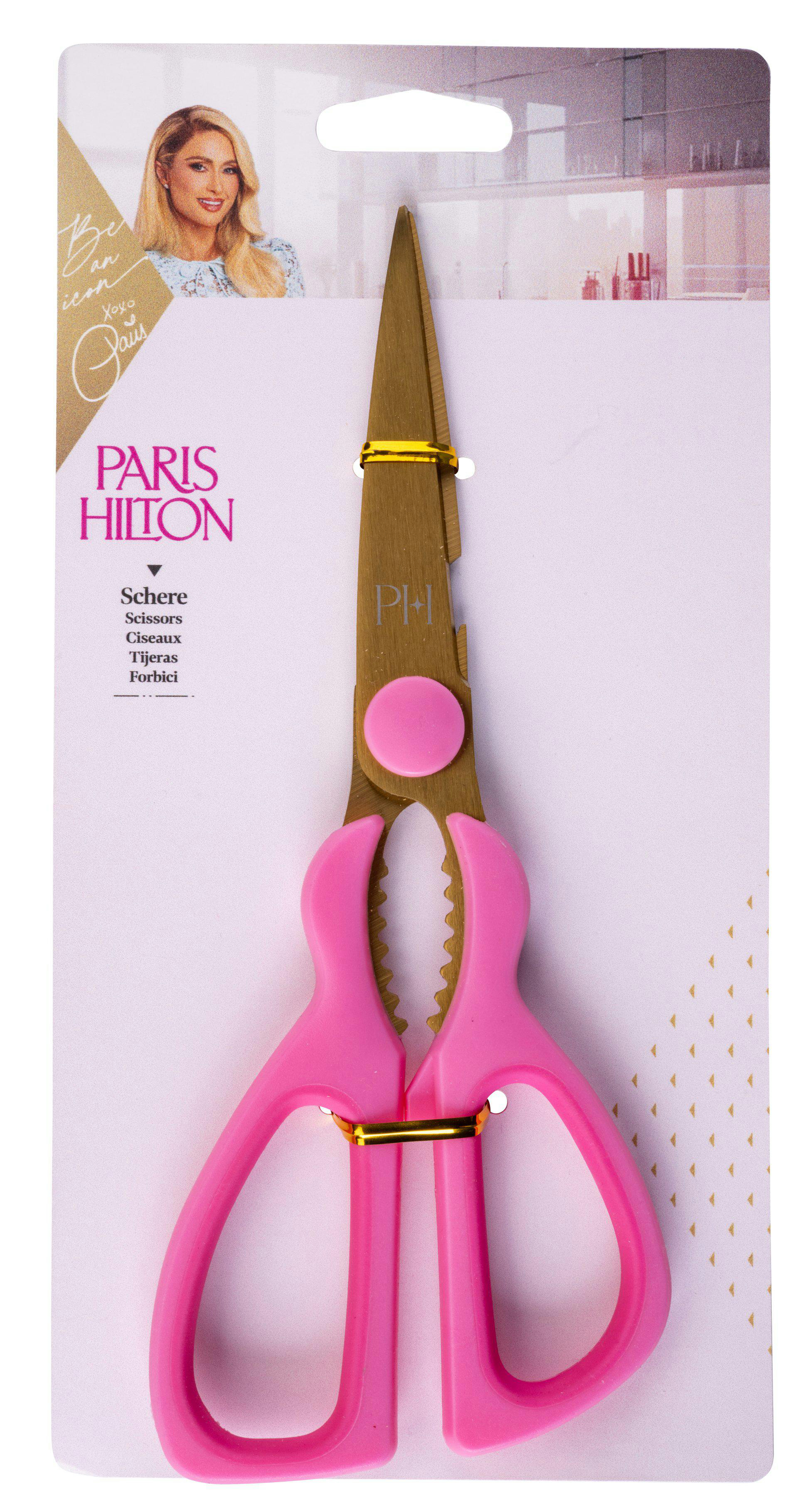 Rosa-goldene Schere auf rosa-weißem Hintergrund. Paris Hilton-Branding oben. Die Schere befindet sich in einer Verpackung.