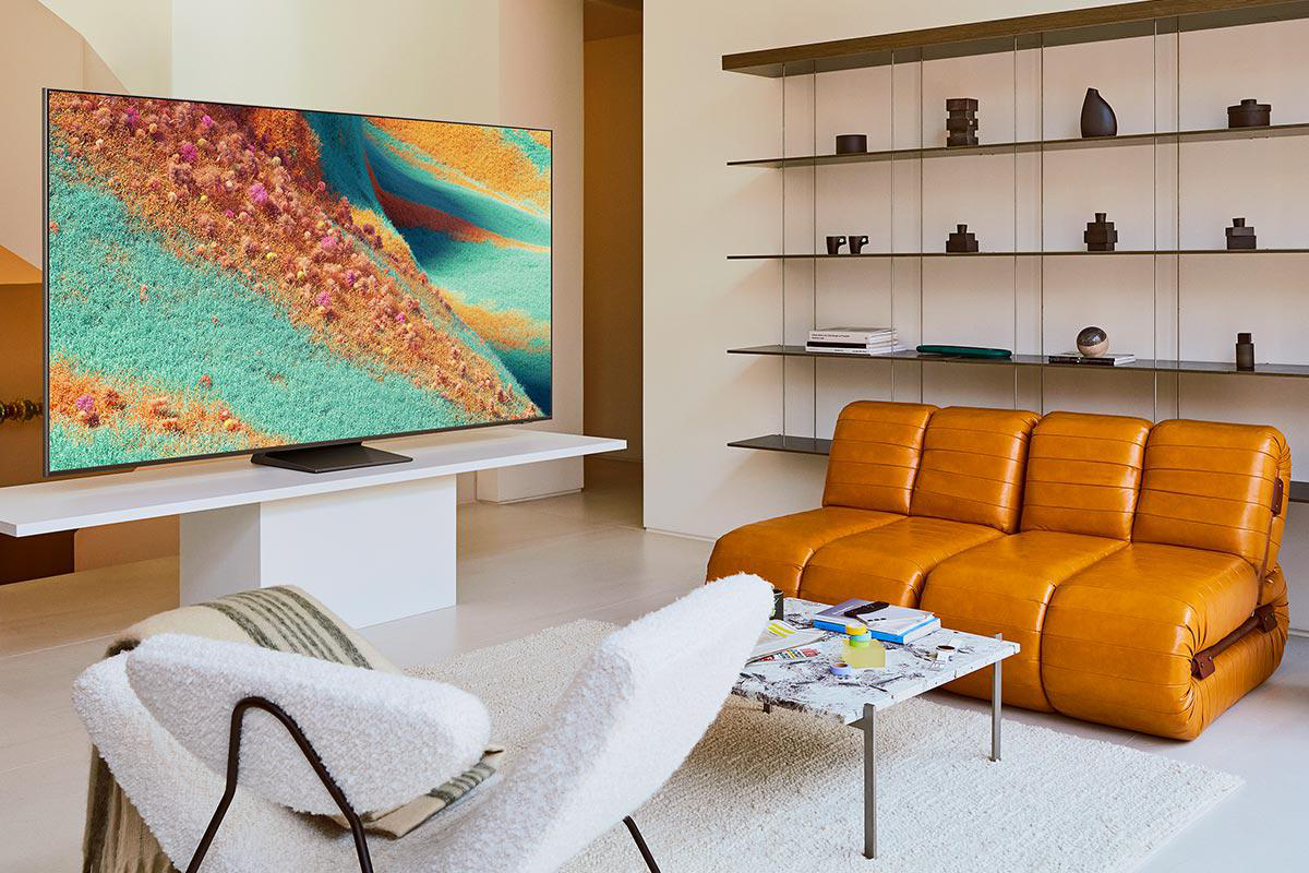 Wohnzimmer mit TV-Gerät, das abstrakte Kunst zeigt, orangefarbenes Ledersofa, weißer Stuhl, Couchtisch und Wandregale.