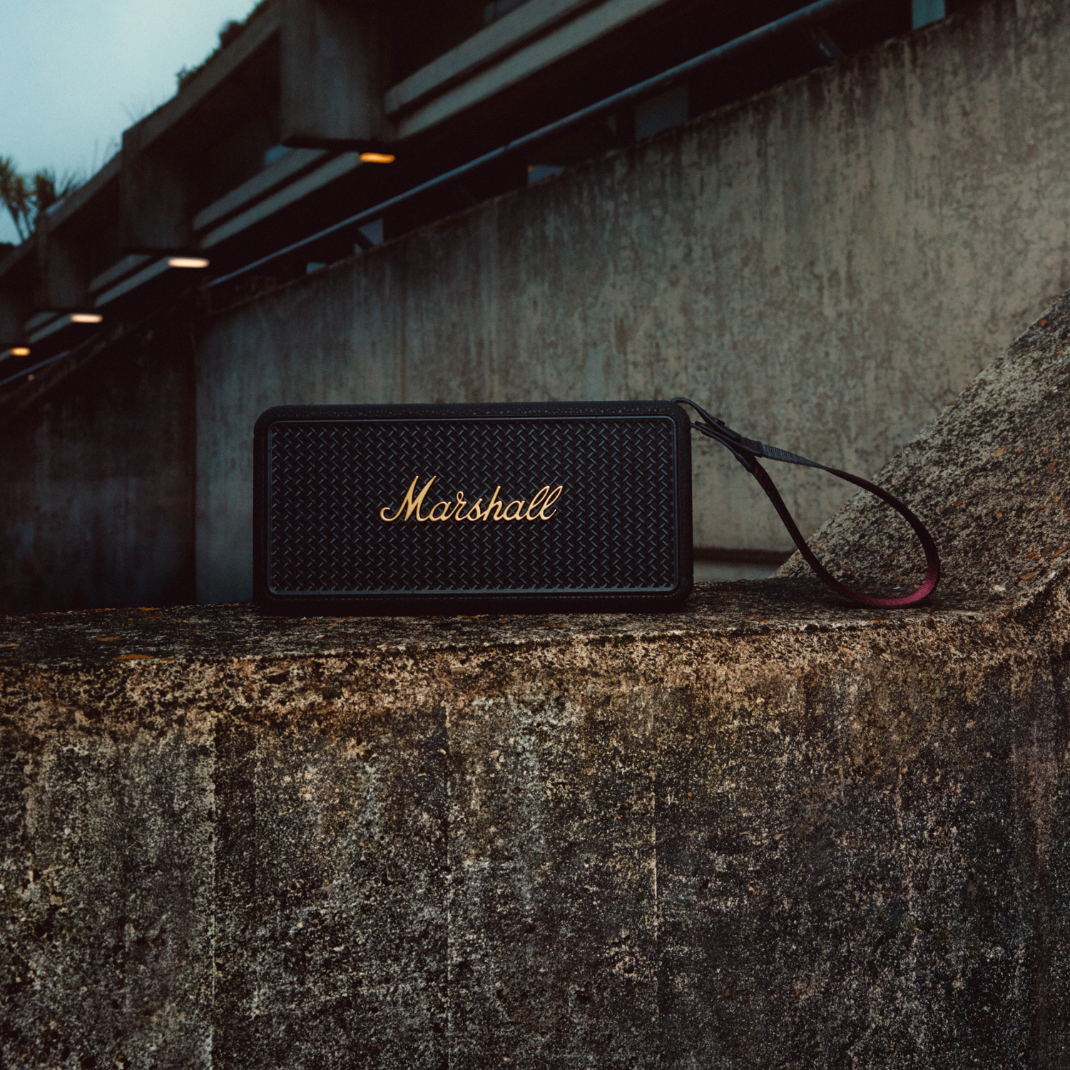 Zwarte Marshall-luidspreker op beton. Gouden Marshall-logo en zwarte band. Achtergrond is een gebouw.