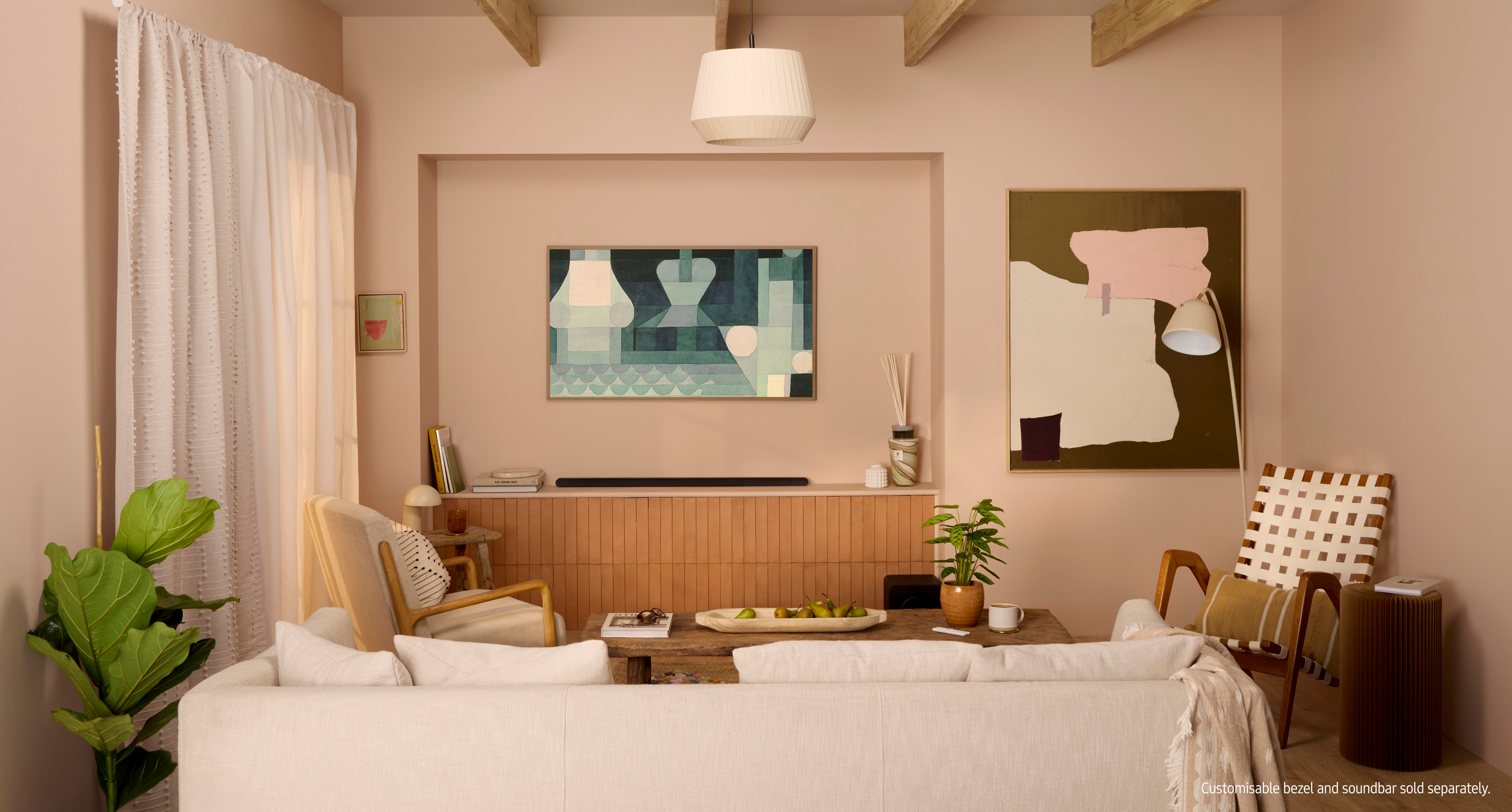 Wohnzimmer mit beigen Wänden, Fernseher, Sofa und Kunst. Ein Couchtisch mit Obst steht vor dem Sofa. Rechts ist eine Pflanze.