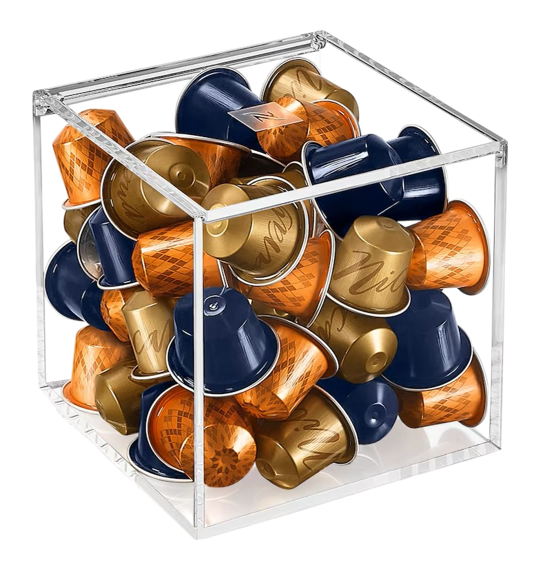 Ein klarer Würfel gefüllt mit Kaffeekapseln. Die Kapseln sind gold, orange und marineblau. Der Hintergrund ist schwarz.