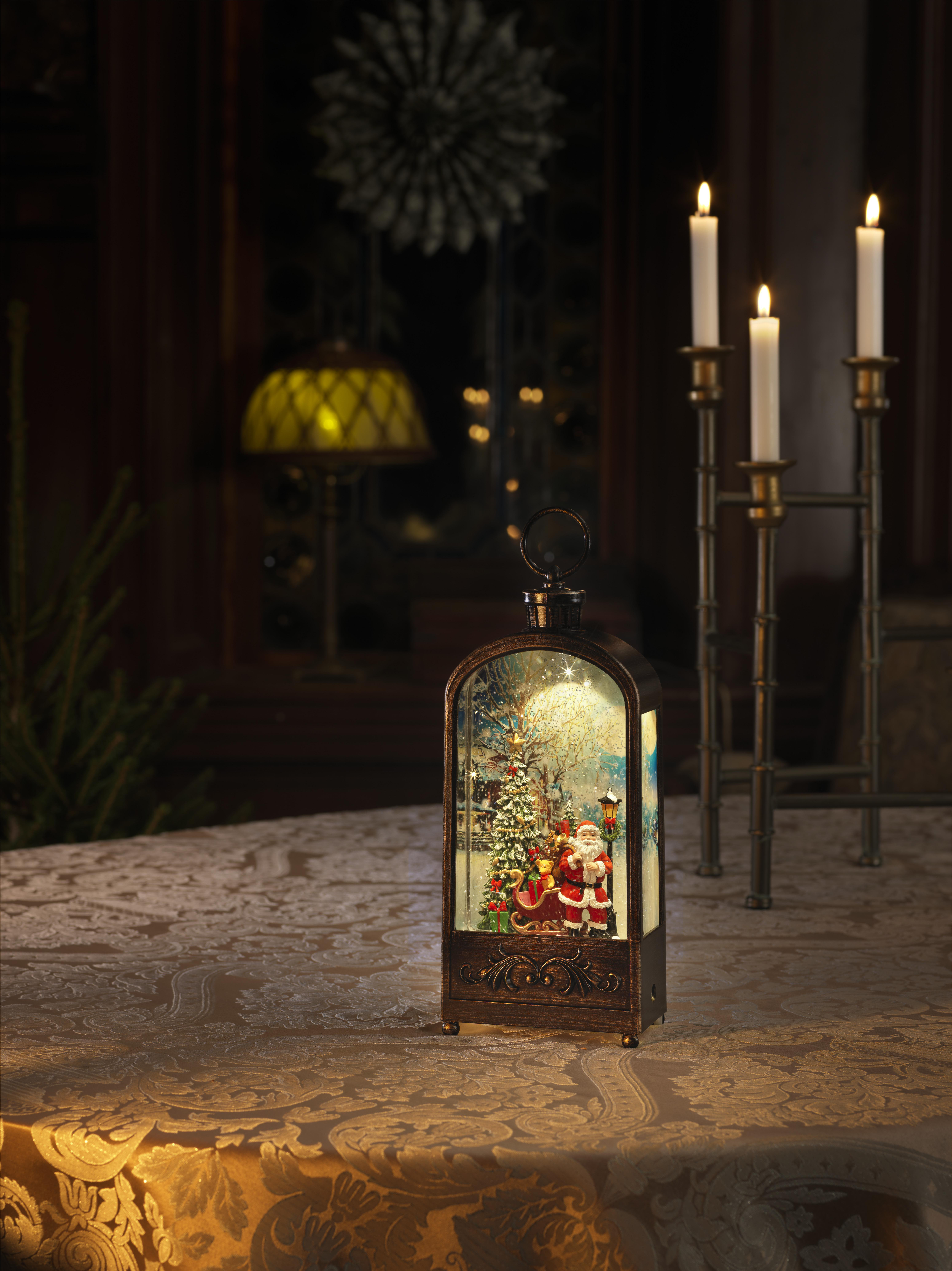 Eine Weihnachtsszene in einer Laterne mit Weihnachtsmann, Schlitten und Weihnachtsbaum, brennenden Kerzen und einem gemusterten Tisch.