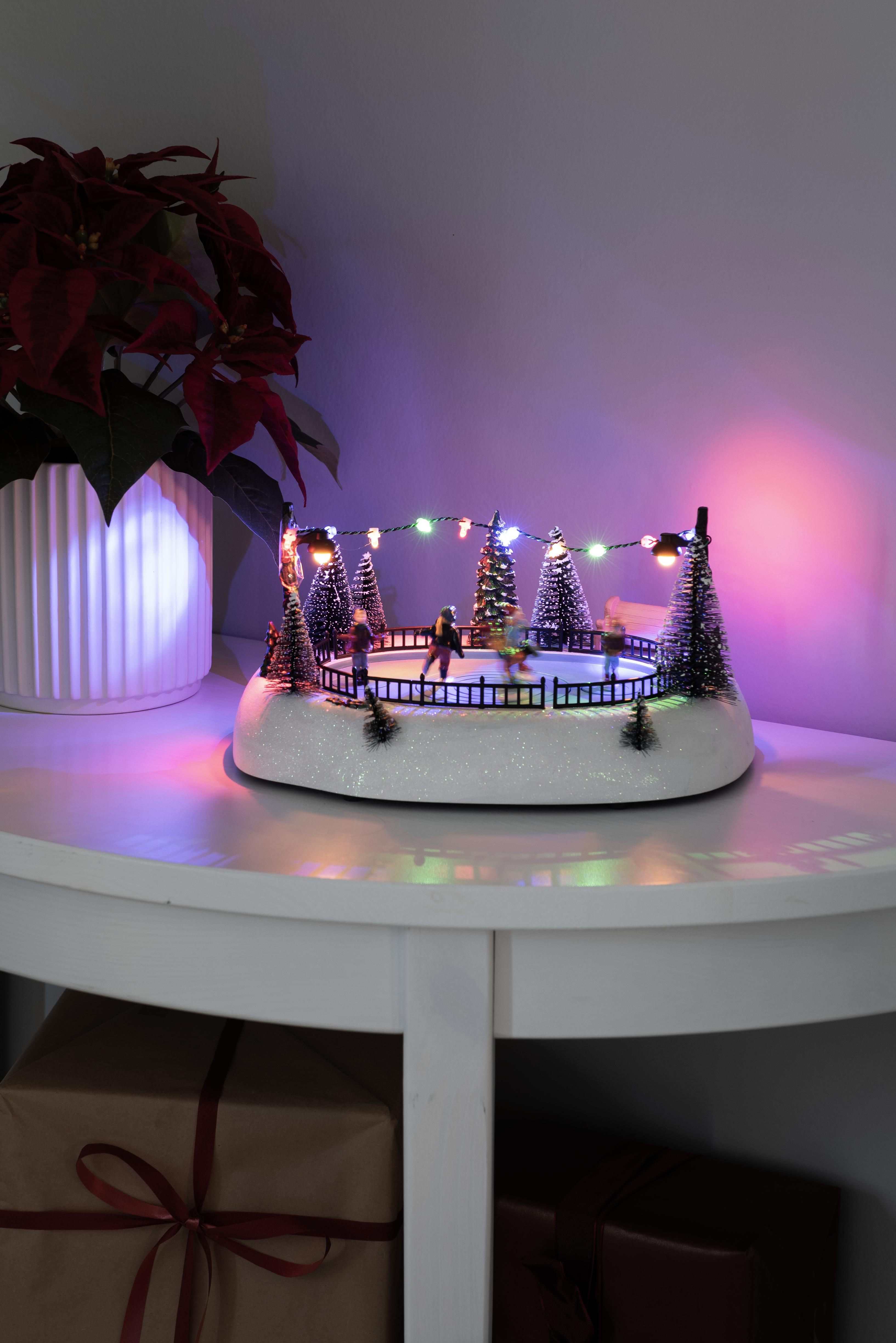 Eine Weihnachtseislaufszene auf einem weißen Tisch. Links ist ein Weihnachtsstern. Geschenke sind darunter.