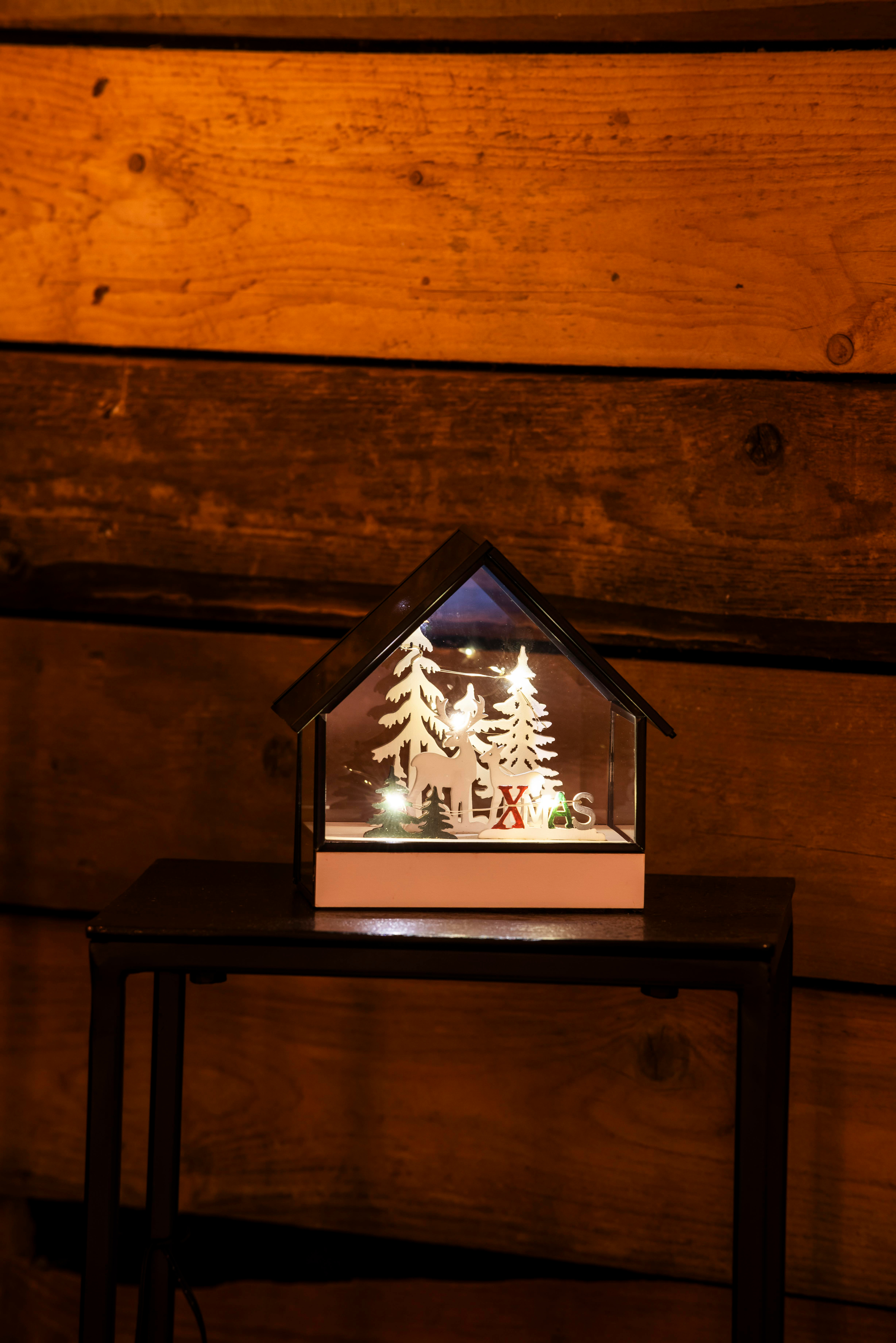 Eine Weihnachtsdekoration, eine hausförmige Box mit Rentieren und Bäumen im Inneren, auf einem schwarzen Tisch, Holz Hintergrund.