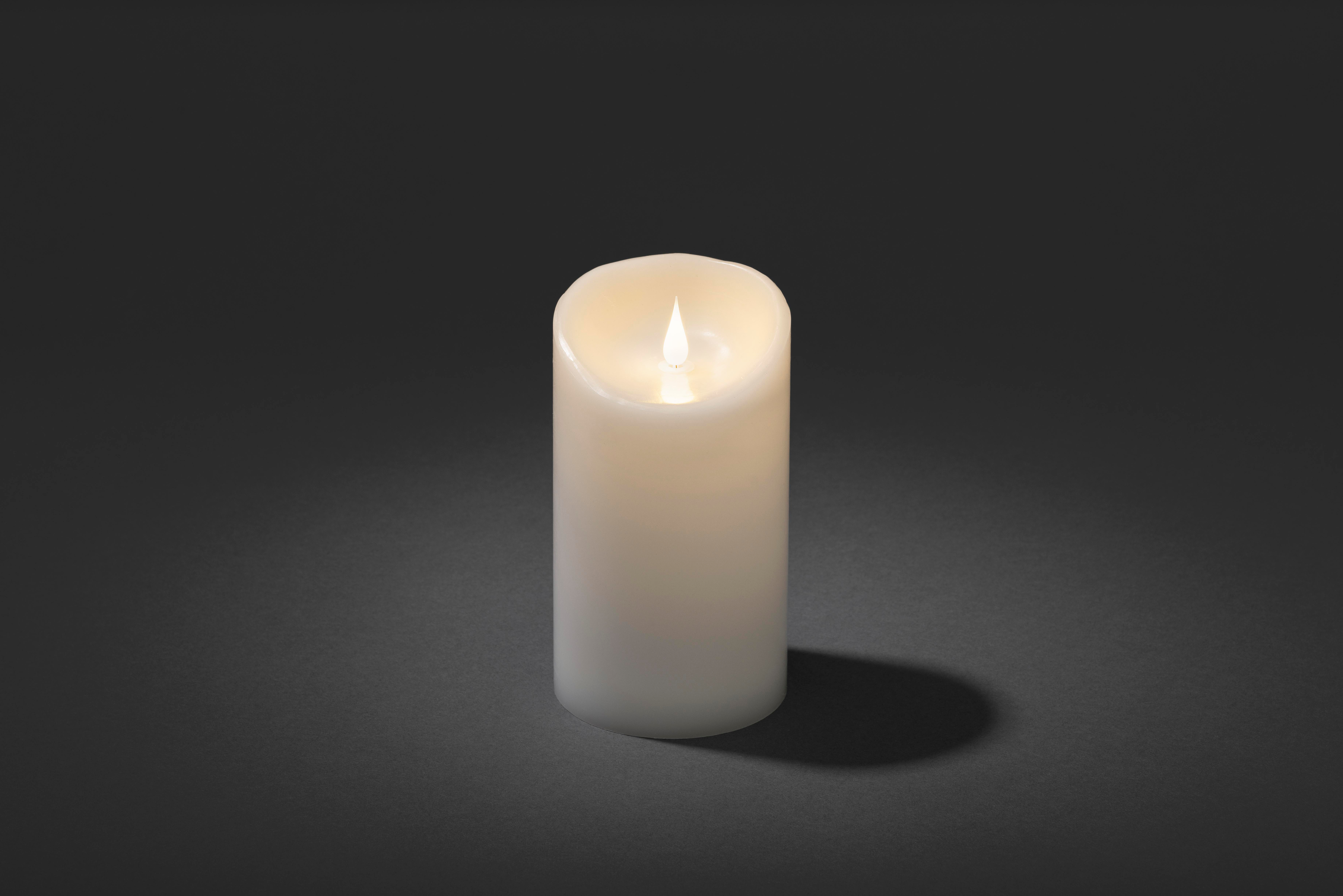 Eine brennende, weiße Kerze steht auf grauem Untergrund. Die Flamme leuchtet vor dunklem Hintergrund. Ein Schatten.