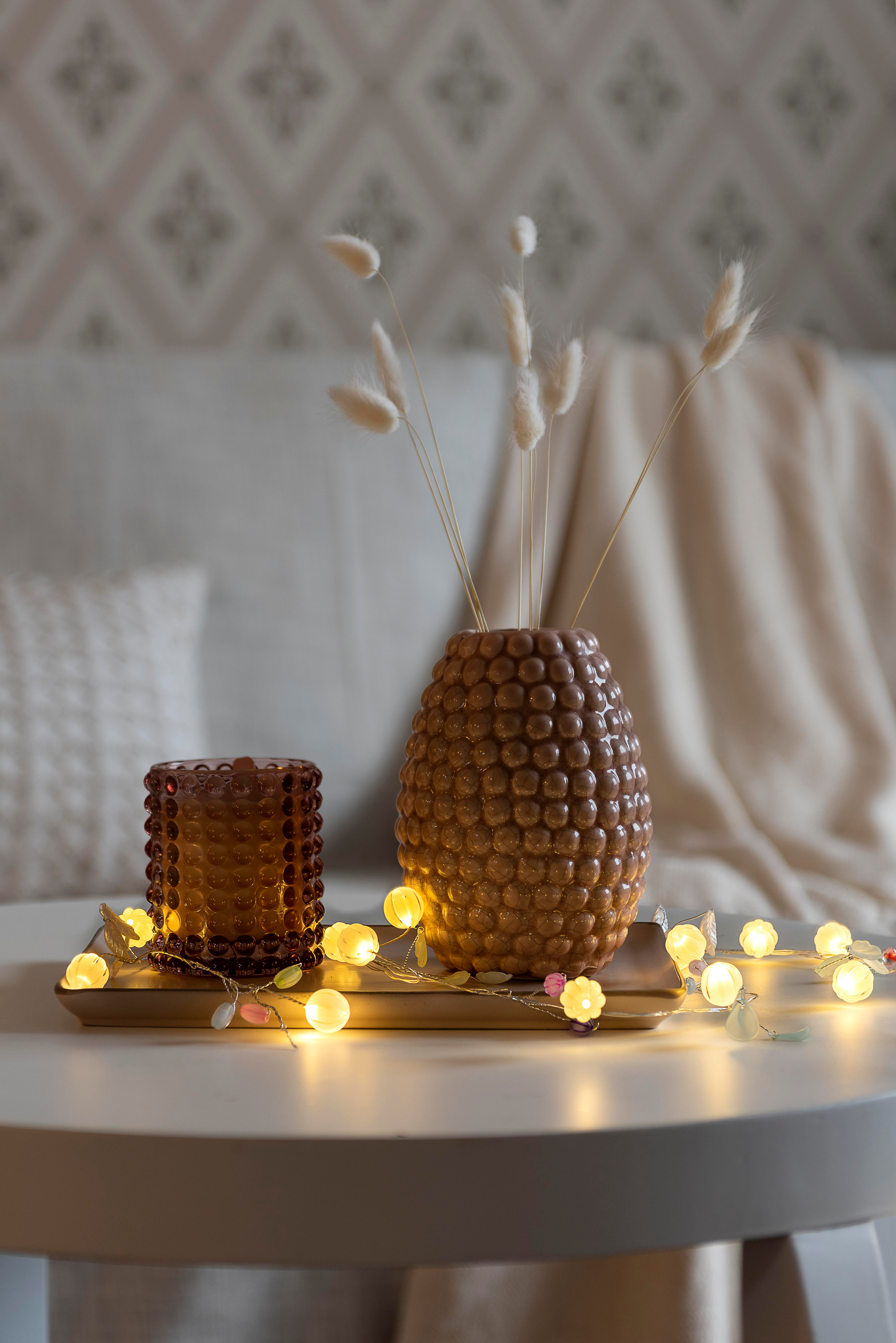 Ein Tisch mit Vase und Trockenblumen, Kerzenhalter und Lichterkette. Im Hintergrund ein Sofa mit Kissen.