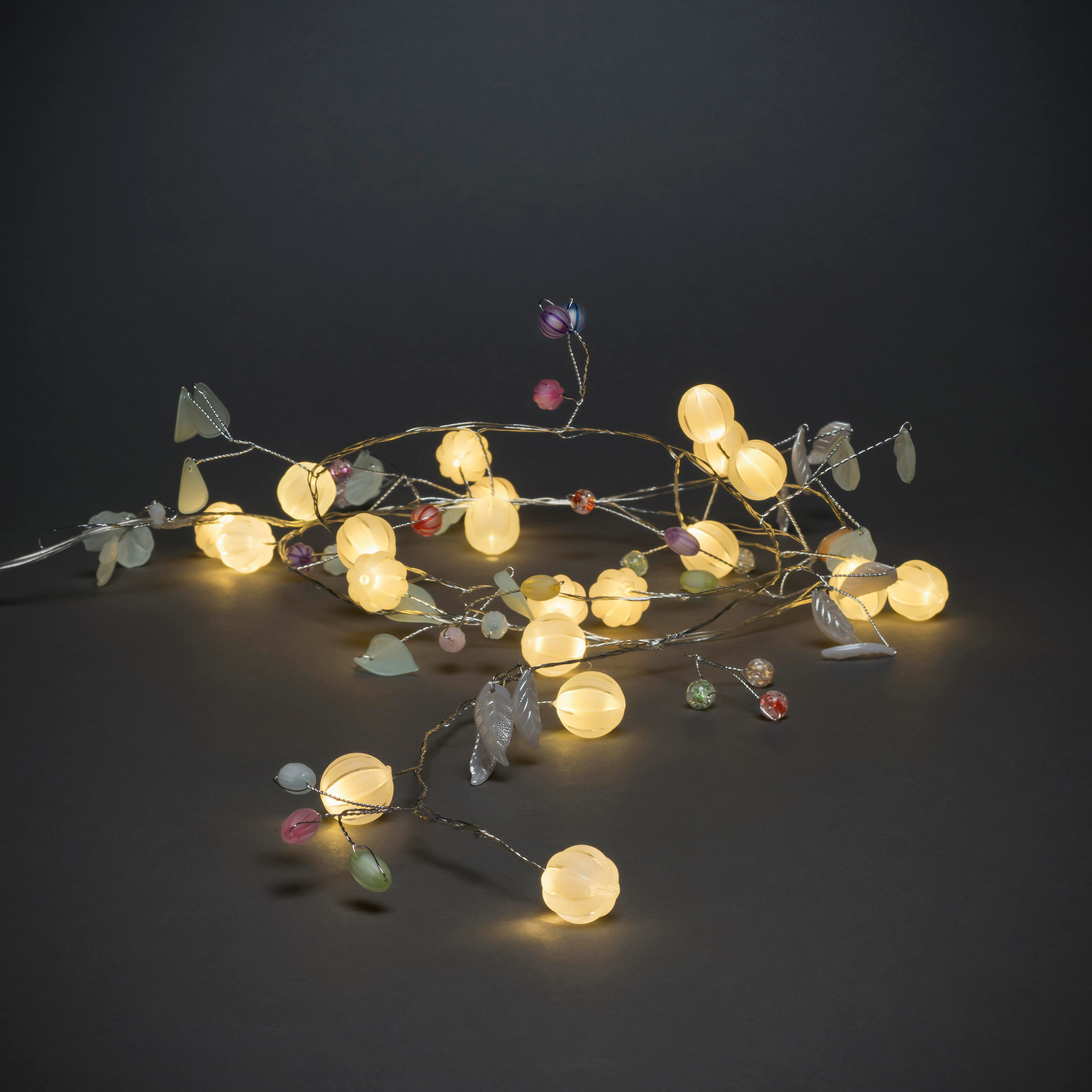 Lichterkette mit leuchtenden Kugeln, Blättern und bunten Perlen auf dunkler Oberfläche, die eine festliche Atmosphäre erzeugt.
