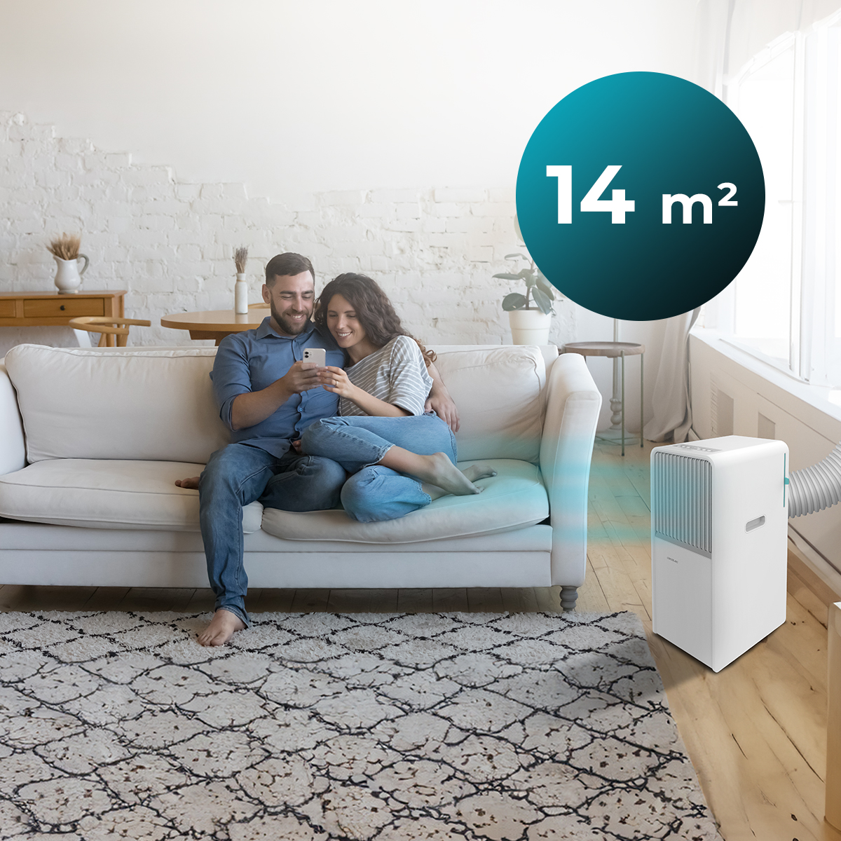 Una pareja sentada en un sofá blanco, mirando un teléfono. Un aire acondicionado portátil está cerca, con un letrero de 14 m².