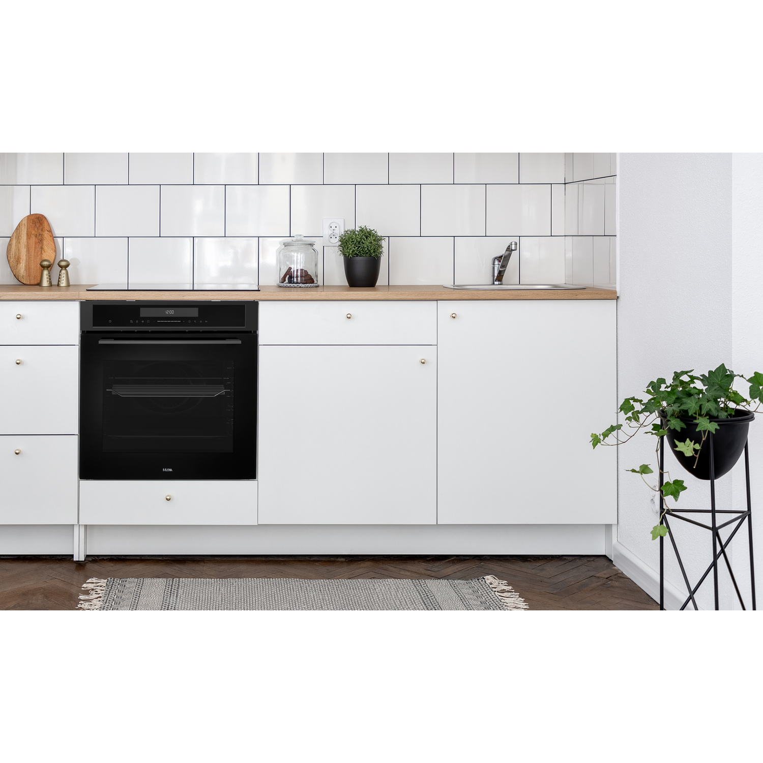 A kitchen with white cabinets, a black oven, and a wooden countertop. A plant with green leaves sits on a stand.