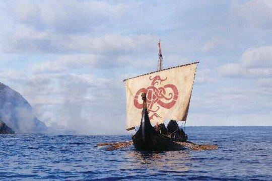 Ein Wikingerschiff segelt auf dem Wasser. Es hat ein rotes Symbol auf dem Segel. Berge und ein bewölkter Himmel sind im Hintergrund.