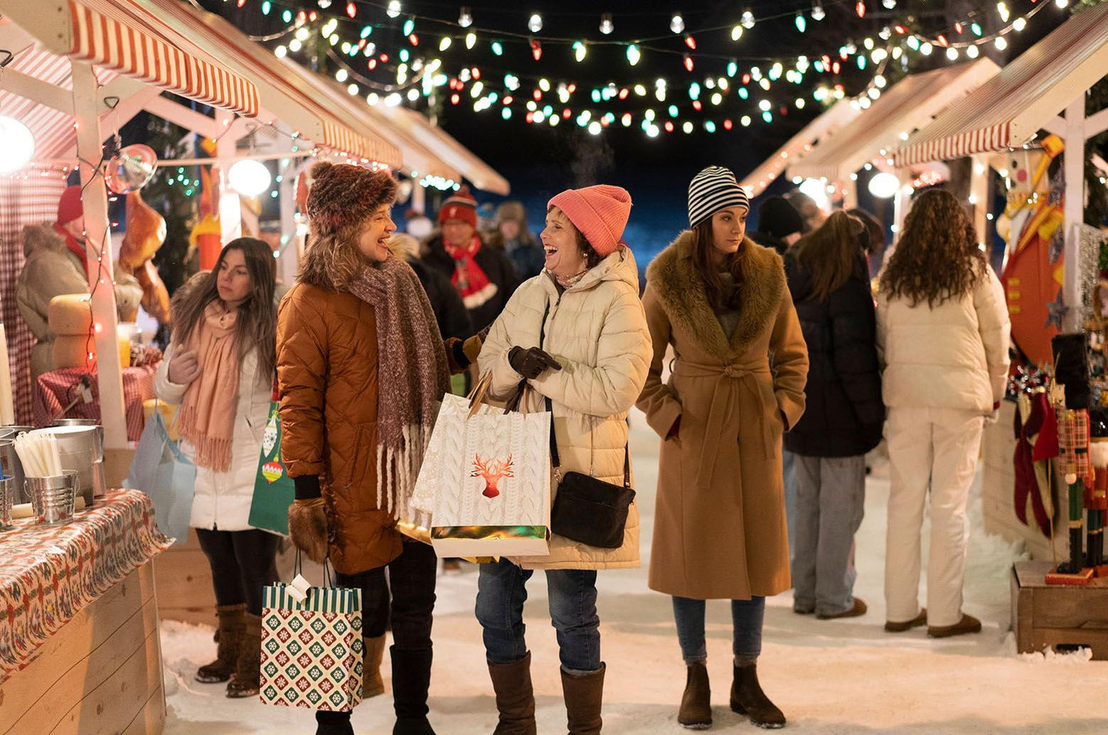 Menschen auf einem Weihnachtsmarkt, die Wintermäntel tragen. Lichter und Marktstände im Hintergrund. Einige Leute tragen Einkaufstaschen.
