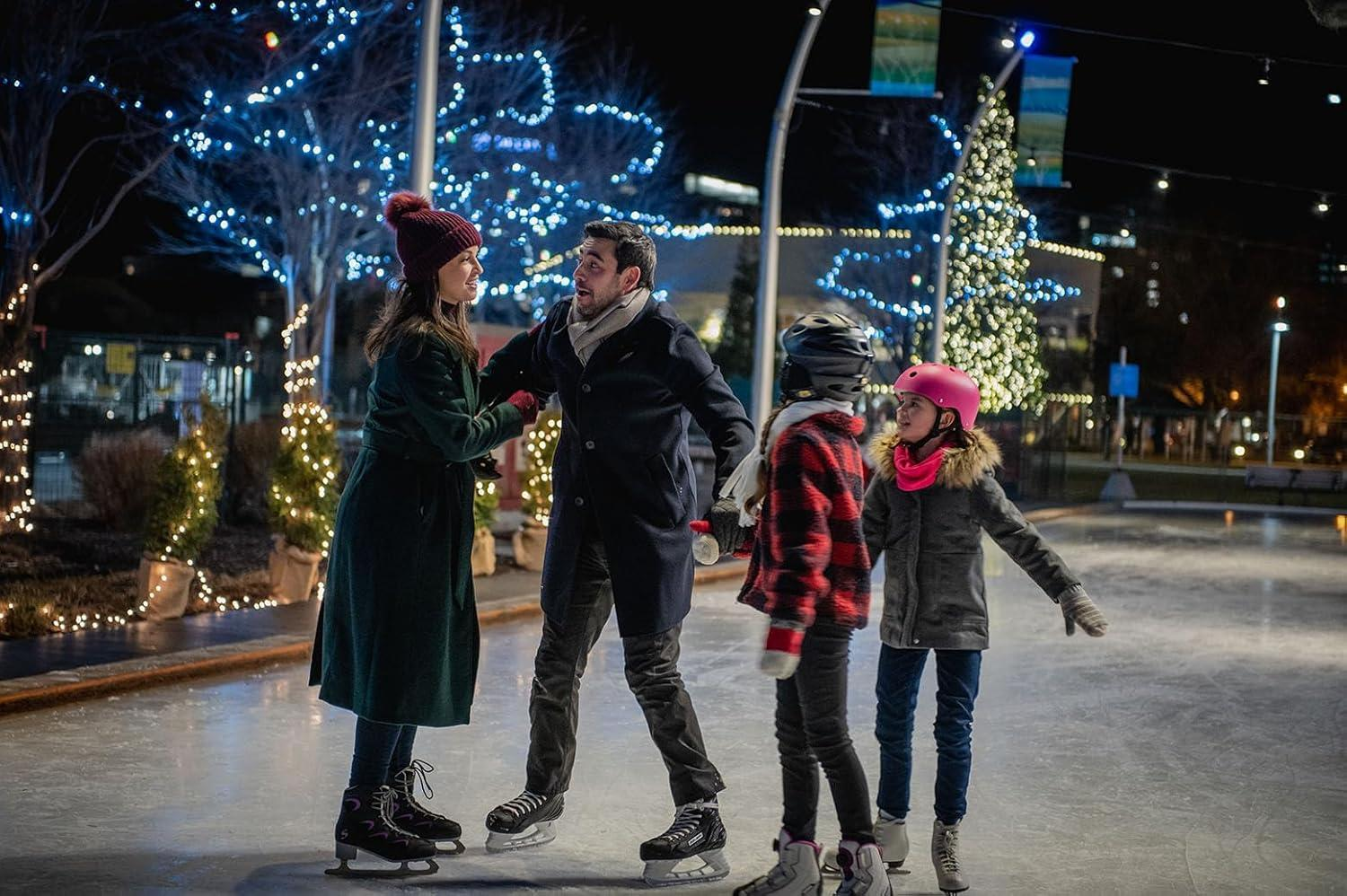 Familien-Eislaufen bei Nacht. Eltern und zwei Kinder auf Schlittschuhen, Weihnachtsbeleuchtung im Hintergrund.