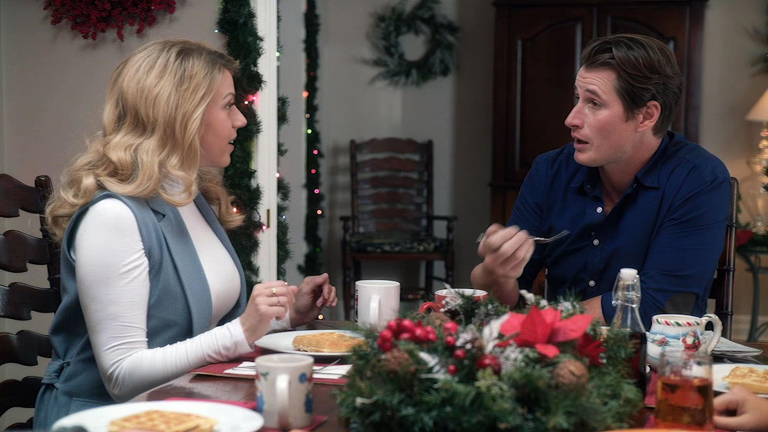 Ein Mann und eine Frau sitzen an einem Tisch mit Essen und Getränken, dekoriert mit Weihnachtsdekorationen.