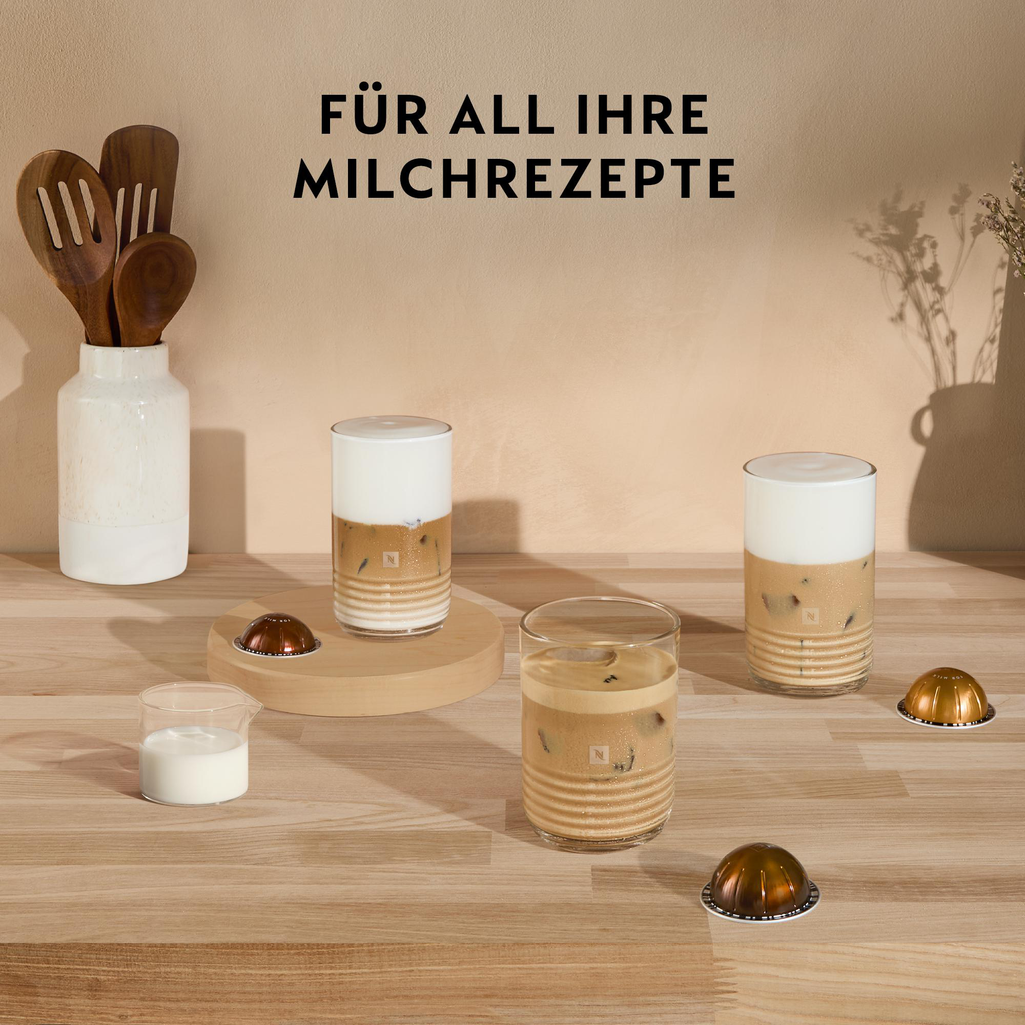 Bild von Kaffeegetränken mit Milch, Kaffeekapseln und Holzutensilien auf einem Holztisch. Text auf Deutsch.