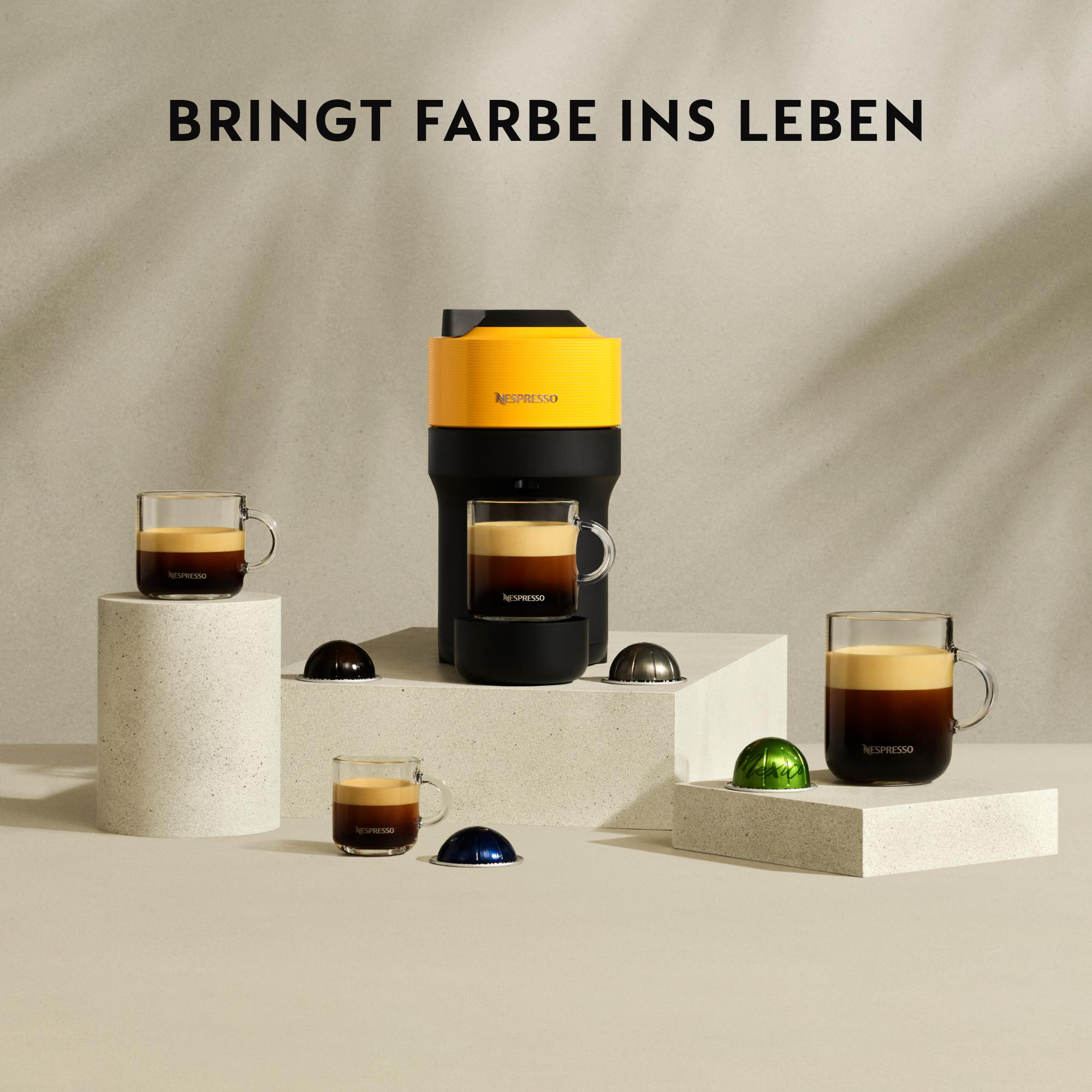 Gelbe und schwarze Nespresso-Maschine mit Kaffeetassen. Kapseln und Text 'BRINGT FARBE INS LEBEN' auf beigem Hintergrund.