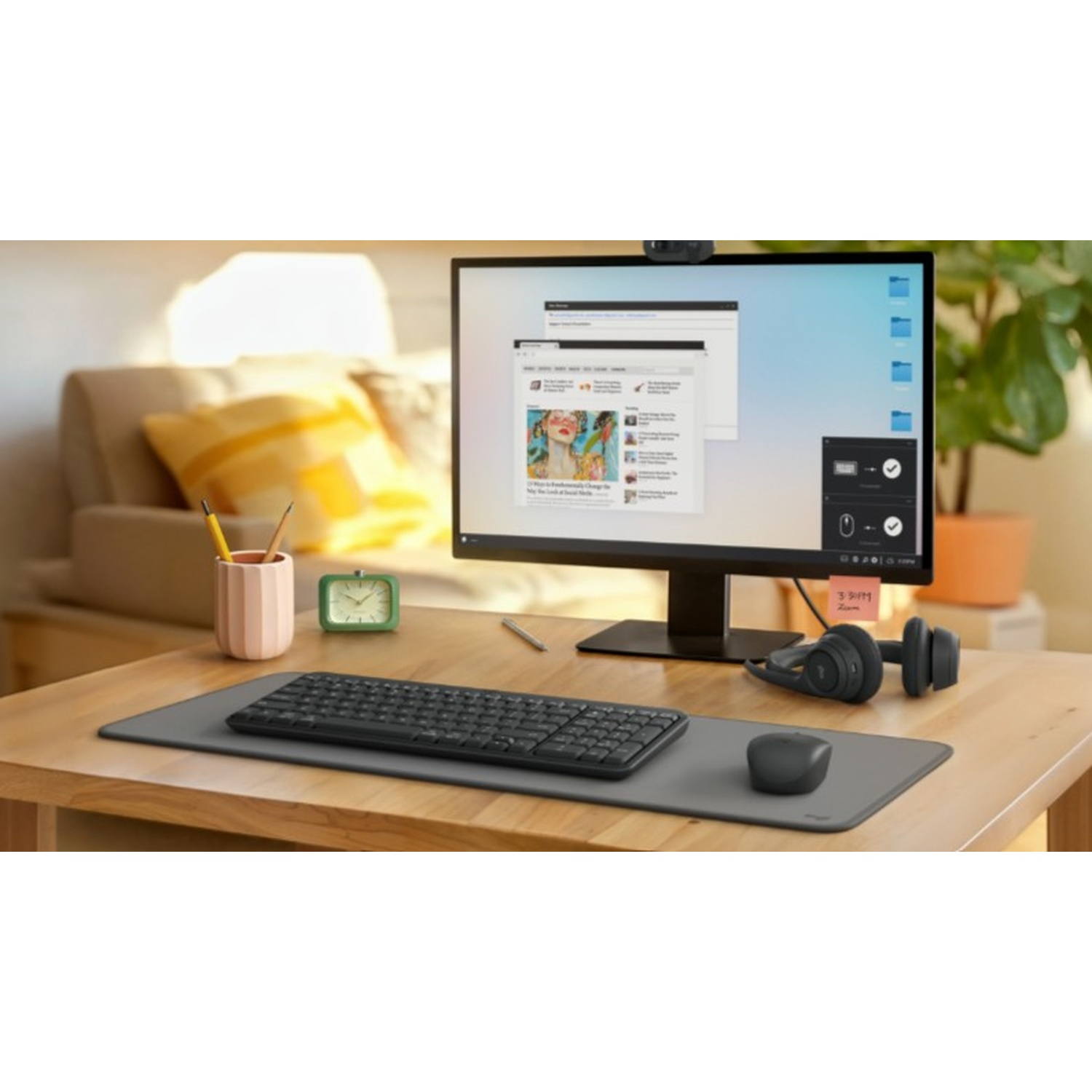 Un'area di lavoro con monitor, tastiera, mouse e cuffie su una scrivania di legno. C'è un orologio e un portapenne.