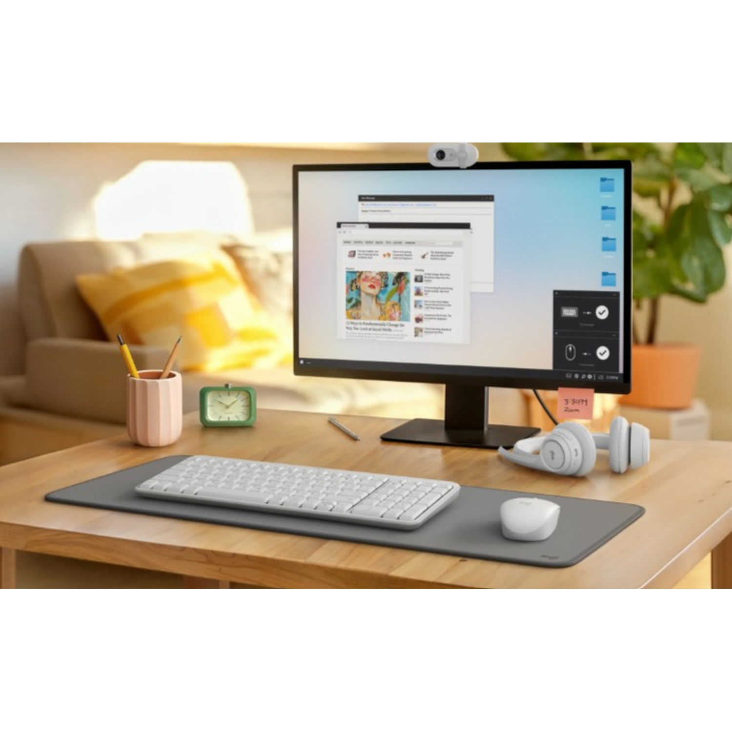 Una scrivania con monitor, tastiera, mouse e cuffie. Sono visibili anche un portapenne, un orologio e una pianta.