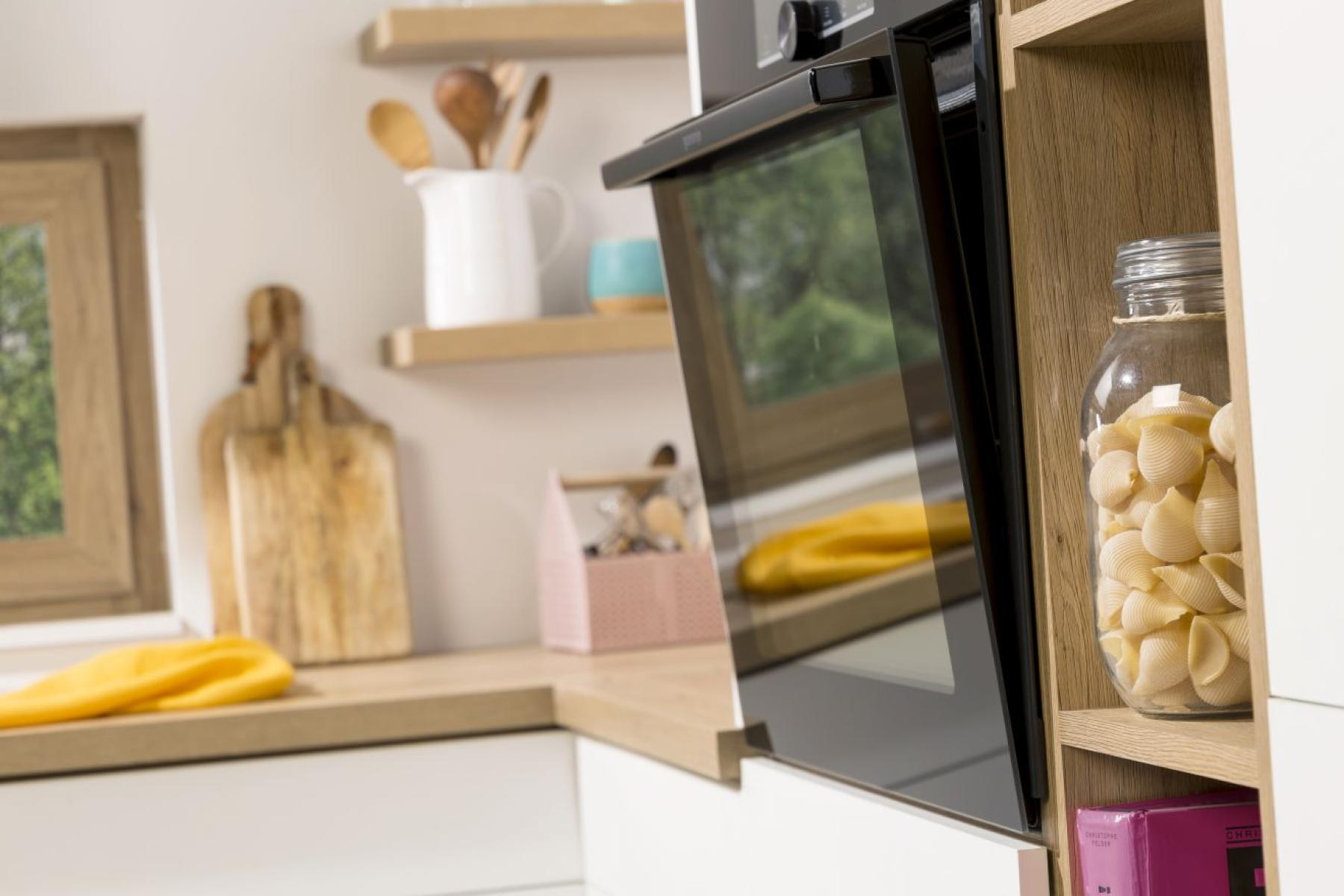 Scena kuchenna z piekarnikiem, słoikiem makaronu i drewnianymi półkami. Zawiera drewnianą deskę do krojenia i okno.
