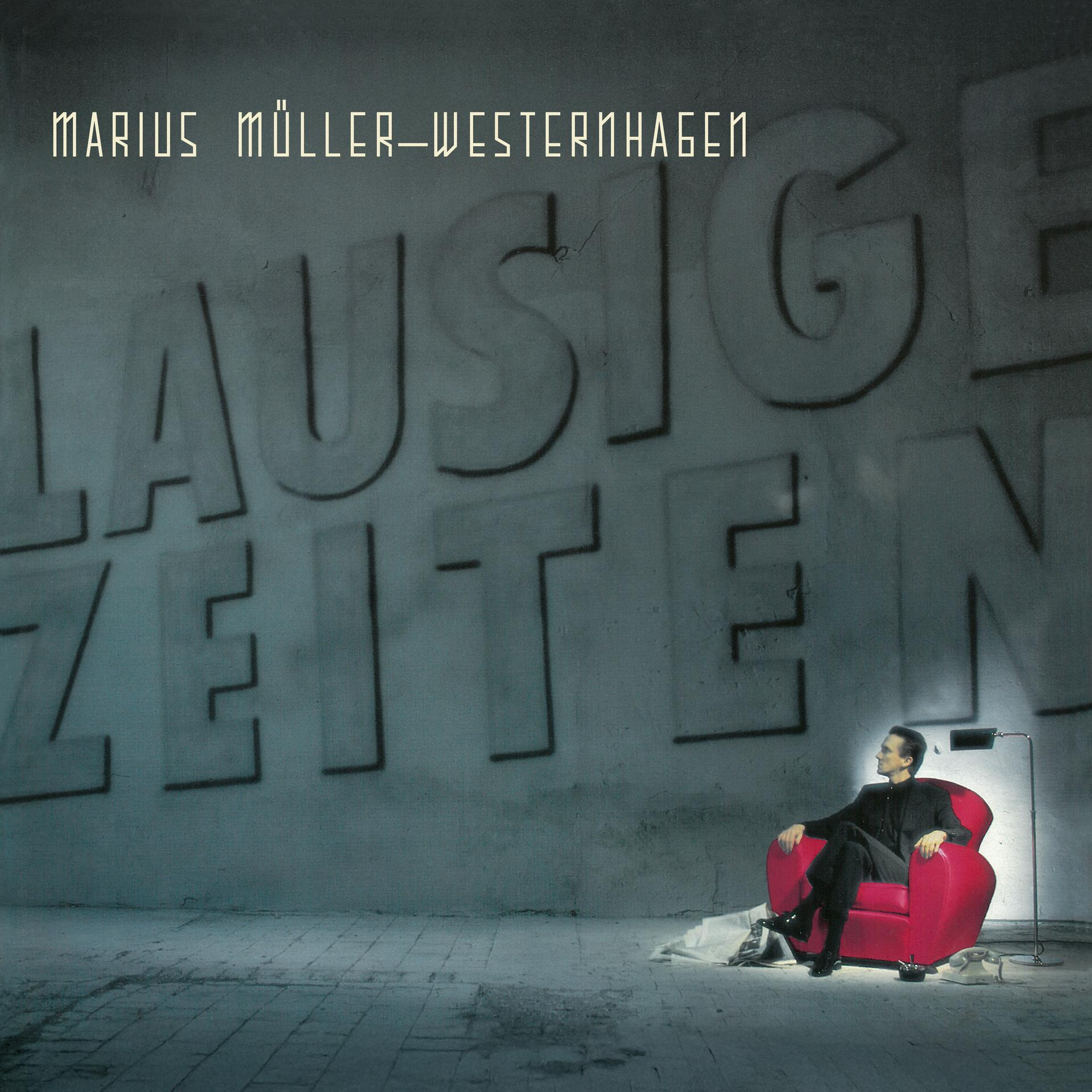Ein Mann sitzt in einem roten Sessel. Große Buchstaben schreiben „LAUSIGE ZEITEN“ an die Wand. Der Name des Künstlers steht oben.