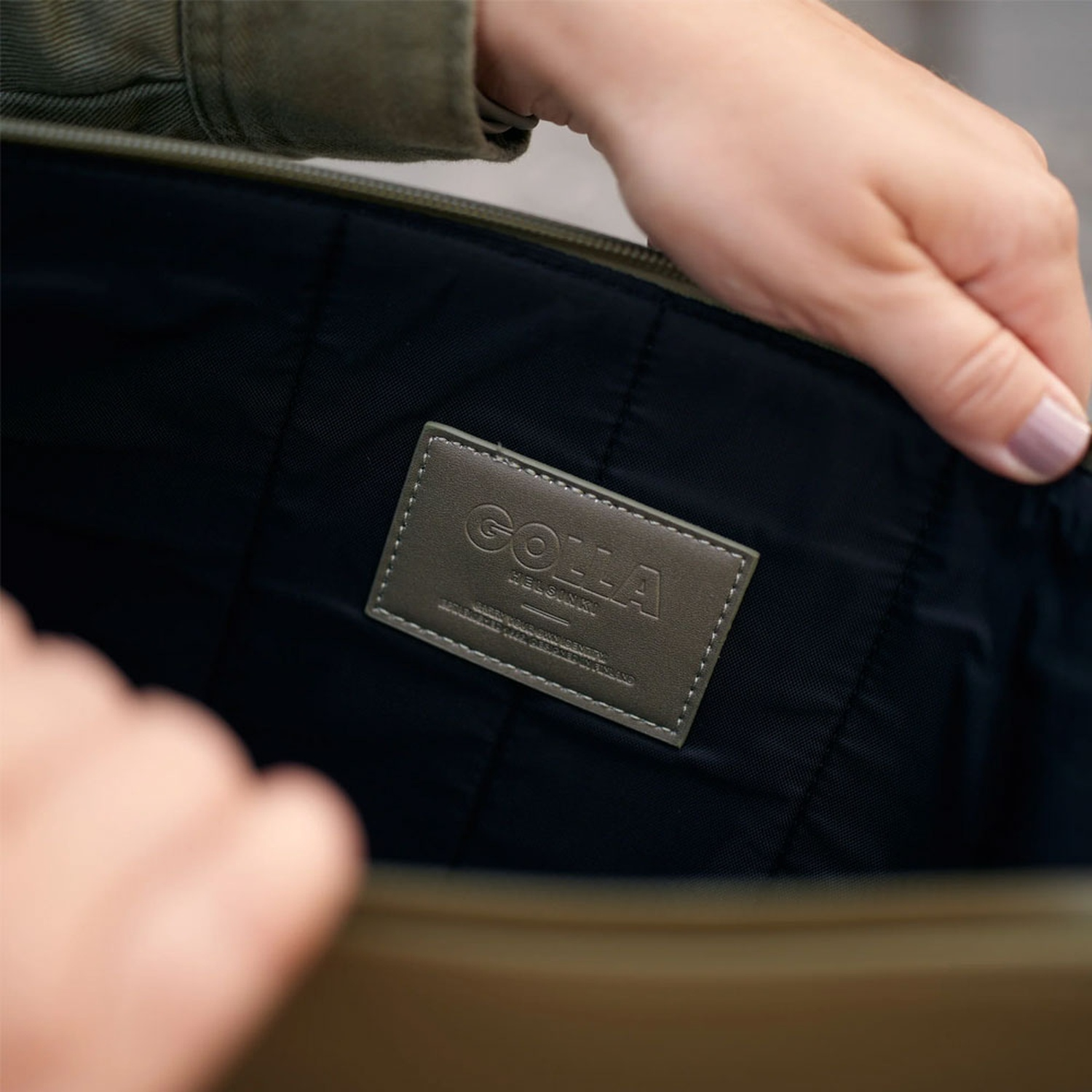Una persona apre una borsa per mostrare l'interno. La borsa è nera con un'etichetta grigia con la scritta GOLLA.