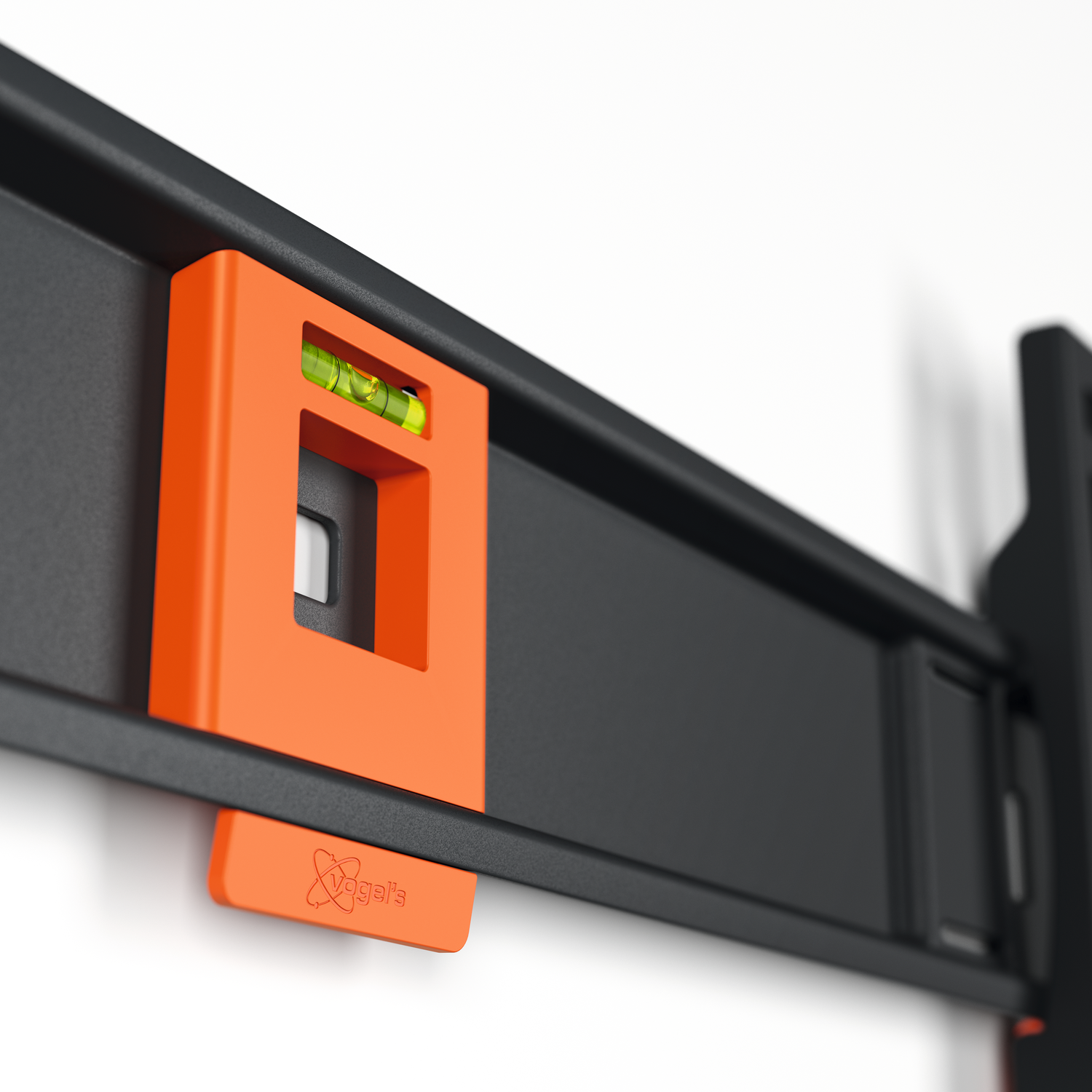 An orange level attached to a black bracket on a white wall. The level has a bubble inside, and the brand name is visible.