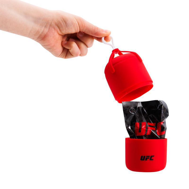 Hand hält einen roten UFC-Behälter, der geöffnet ist und eine schwarze Packung mit UFC-Logo zeigt. Weißer Hintergrund.