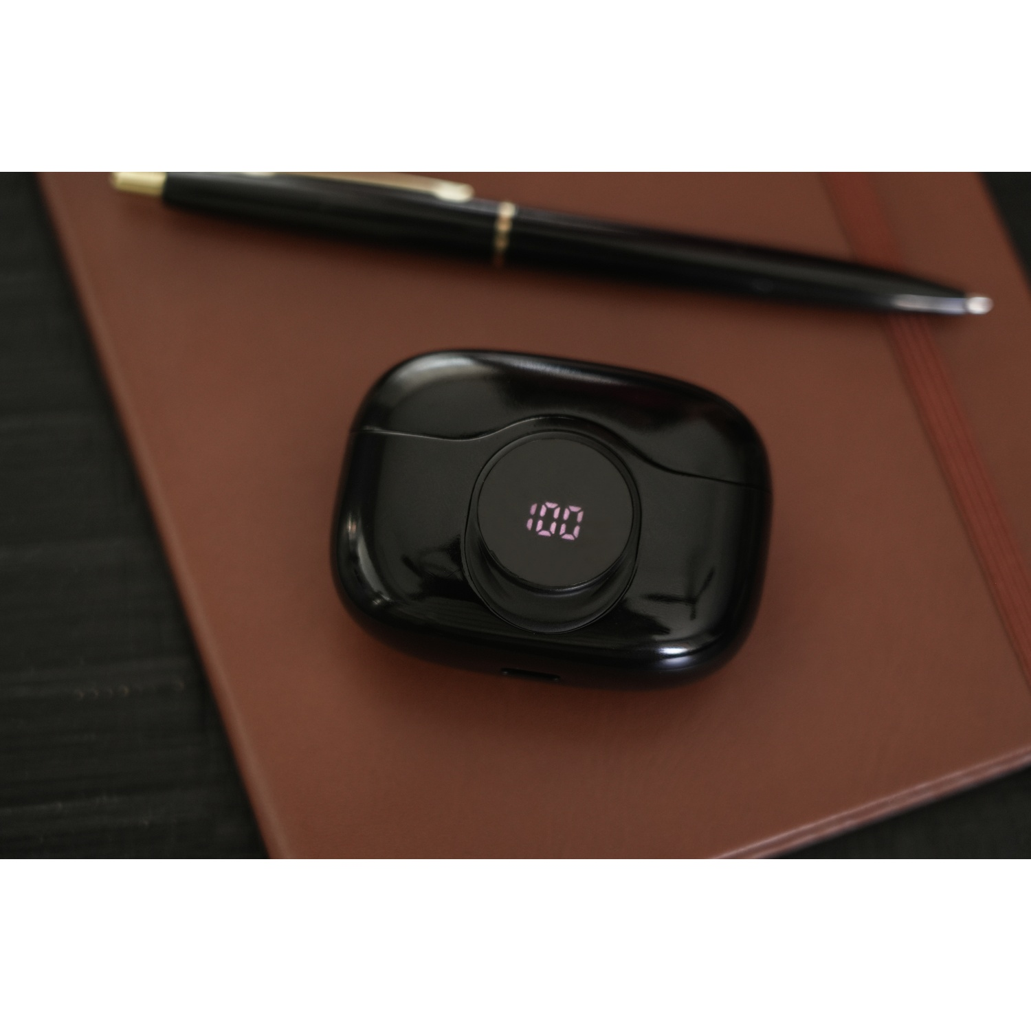 Black earbud case with 100 displayed, pen, and leather notebook.