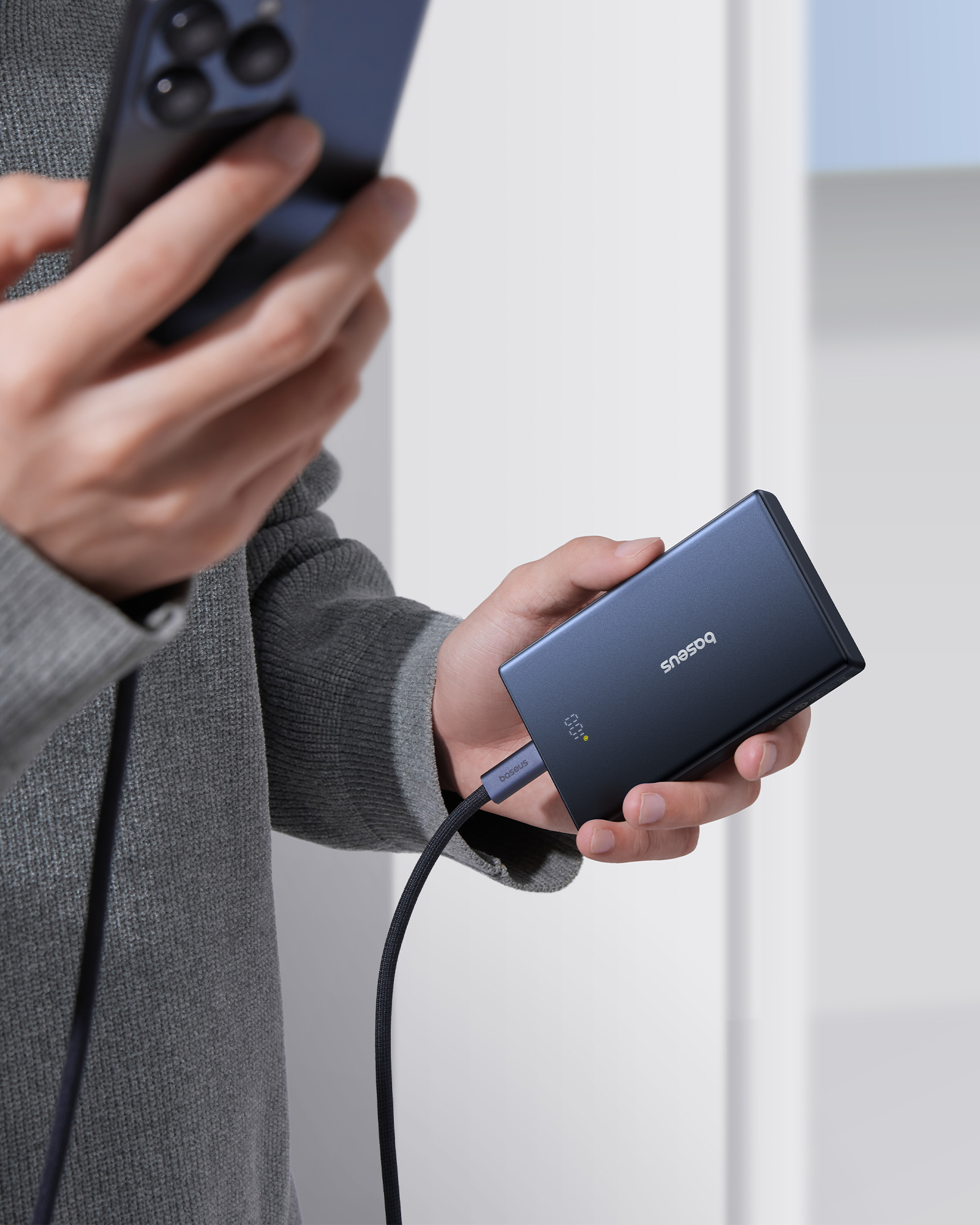 Bir kişi telefon ve koyu mavi bir powerbank tutuyor. Bir kablo onları birbirine bağlar. Powerbank bir yüzde gösterir.